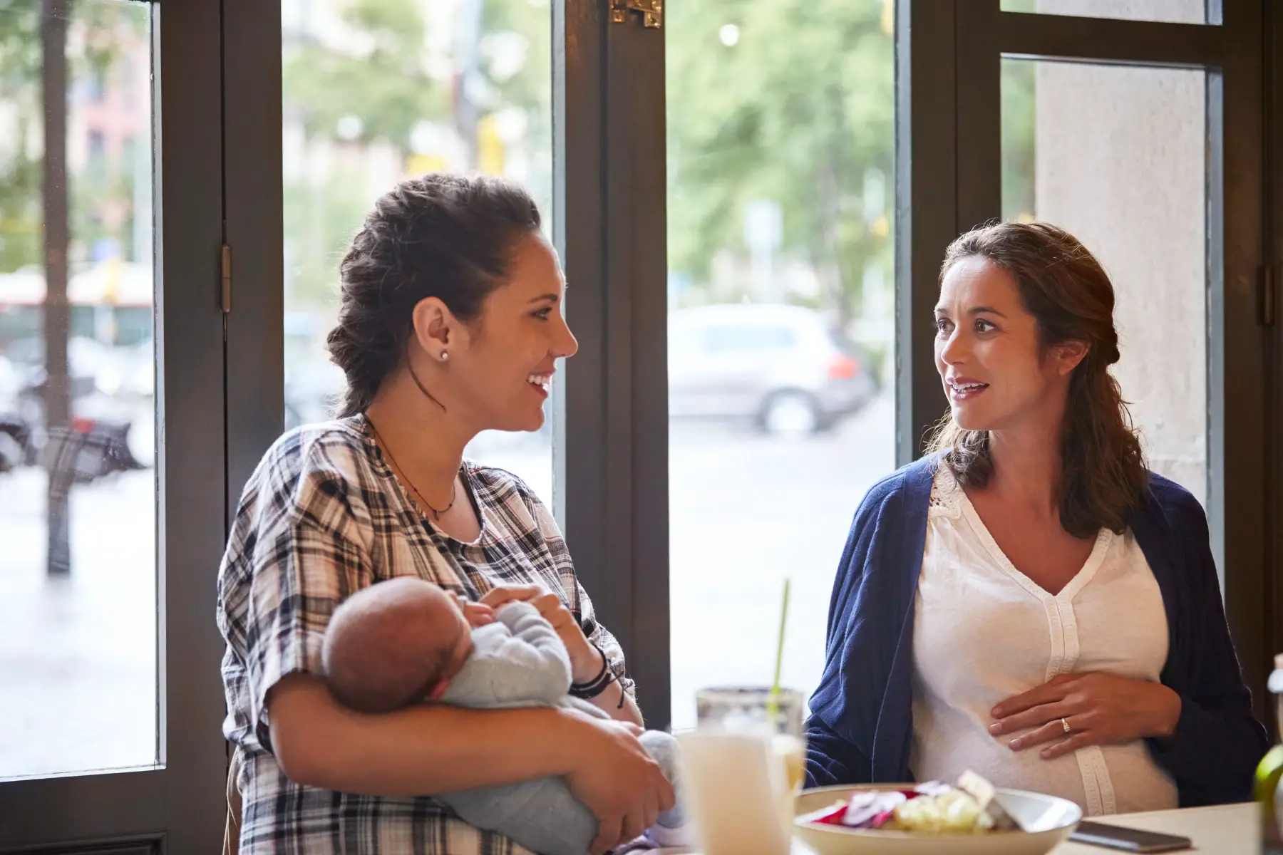 a mother holding her baby as she chats to another mum in a cafe