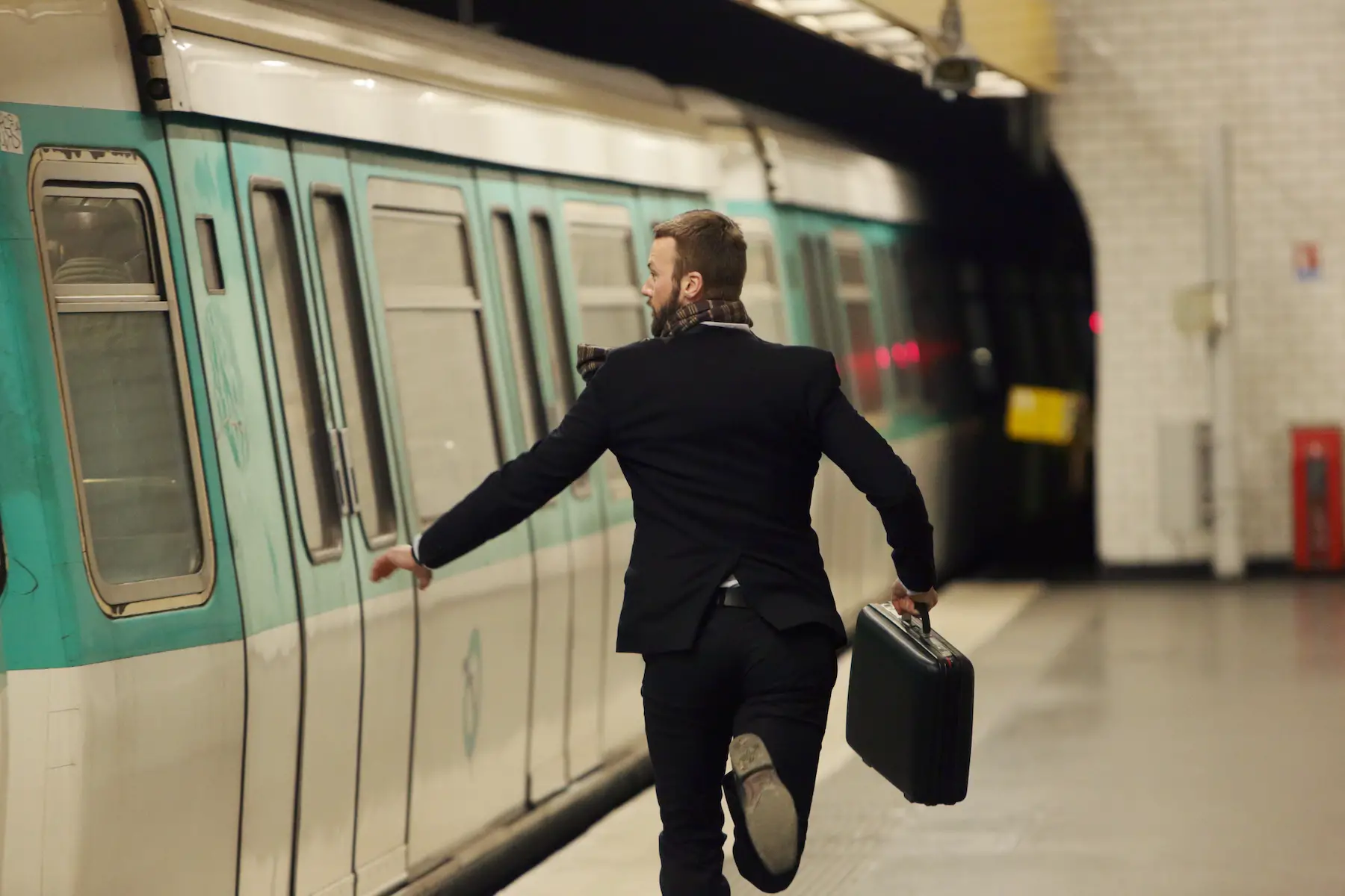 A man in a suit and carrying a briefcase runs to catch a Paris metro train as the doors are closing