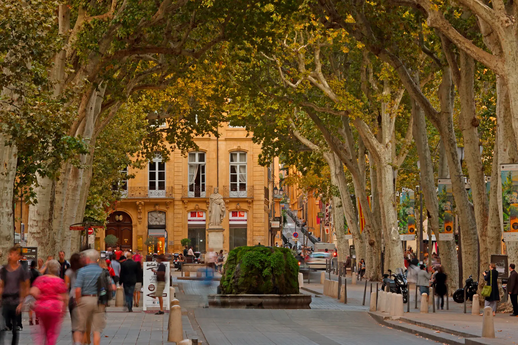 A paved shopping street with people, lined with trees