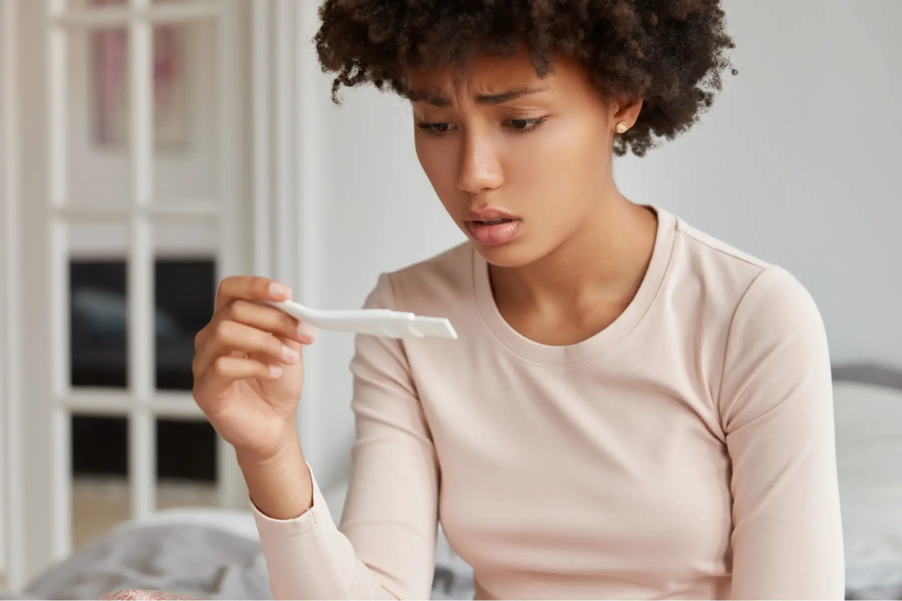Woman looking concerned at pregnancy test; unwanted pregnancy