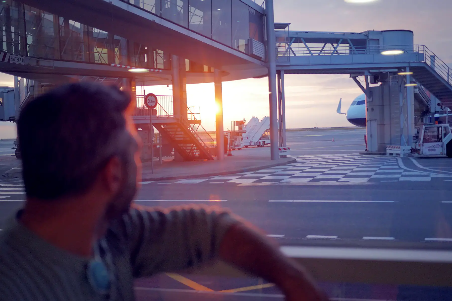 Man looking through airport window at planes at sunset