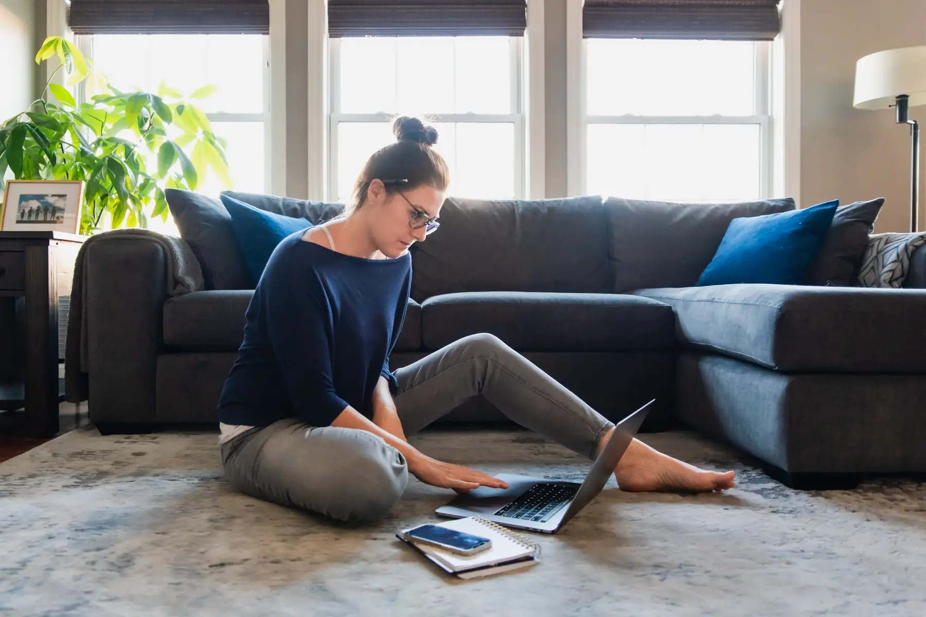 a young woman sitting on the floor in her living room working on a laptop