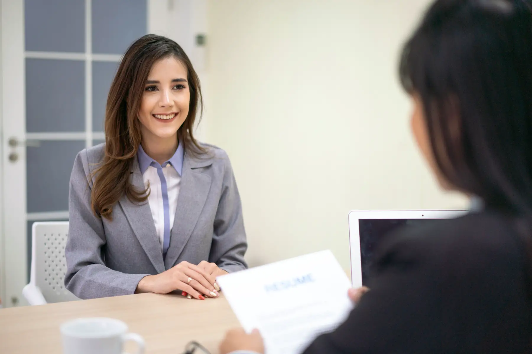 a smiling businesswoman holding a resume and talking to a female candidate during a job interview