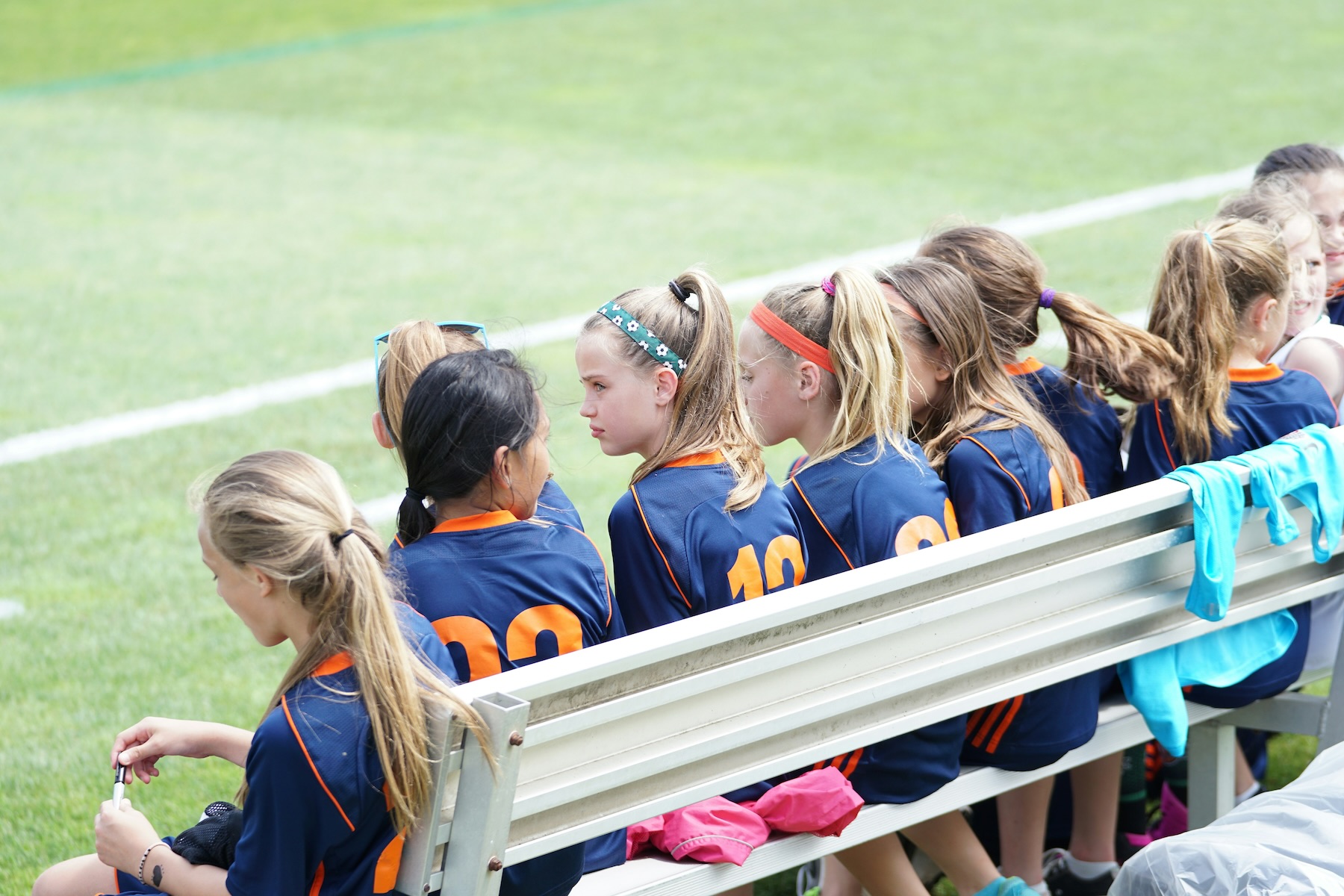 A girls soccer team sits on the bench waiting for the game to start