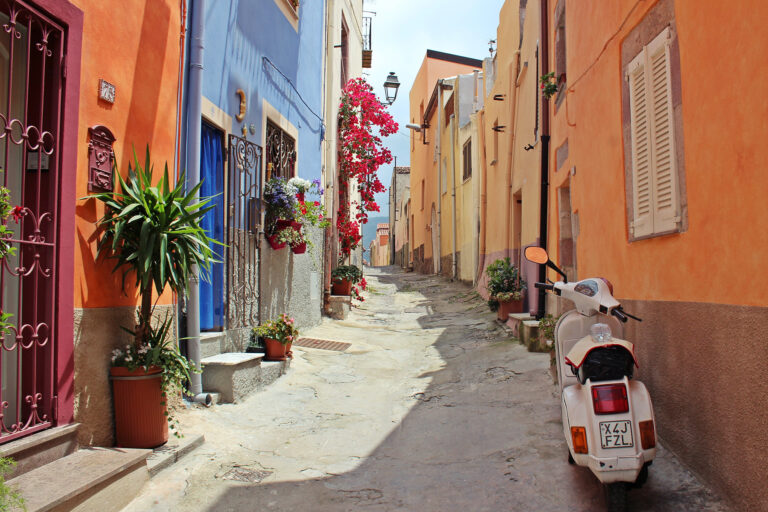 A narrow, sunny street in Italy, with a motorbike parked at the side