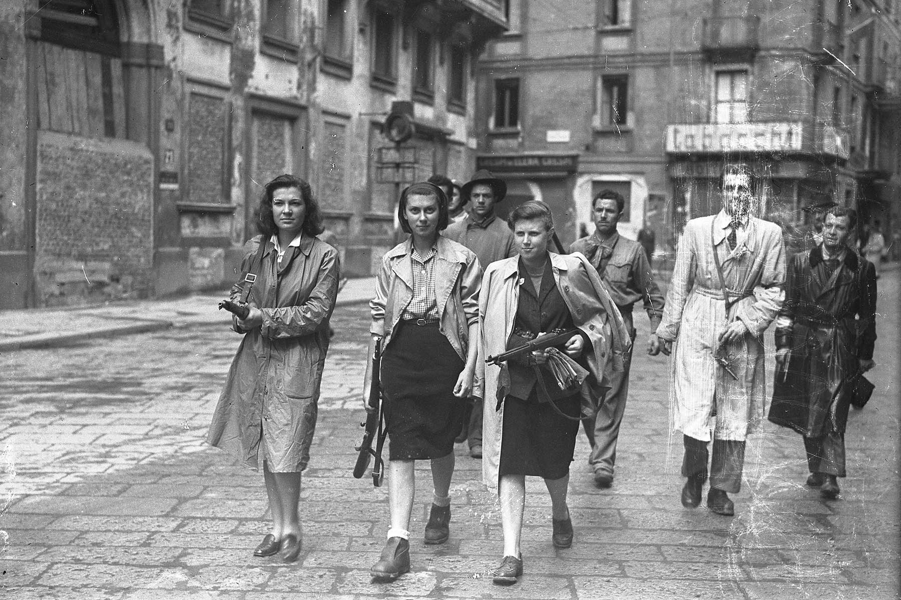 Three unknown women from different social classes walking the streets of Milan, holding weapons to bring and give to the allies after Italy's liberation in 1945.