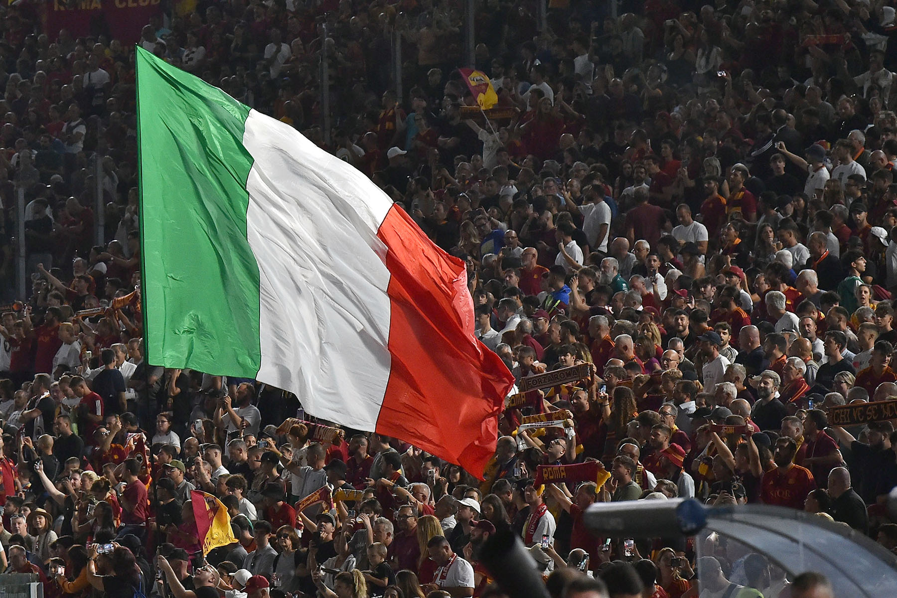 Large Italian flag is flying in a crowd of supporters during a match between AS Roma and AC Milan.