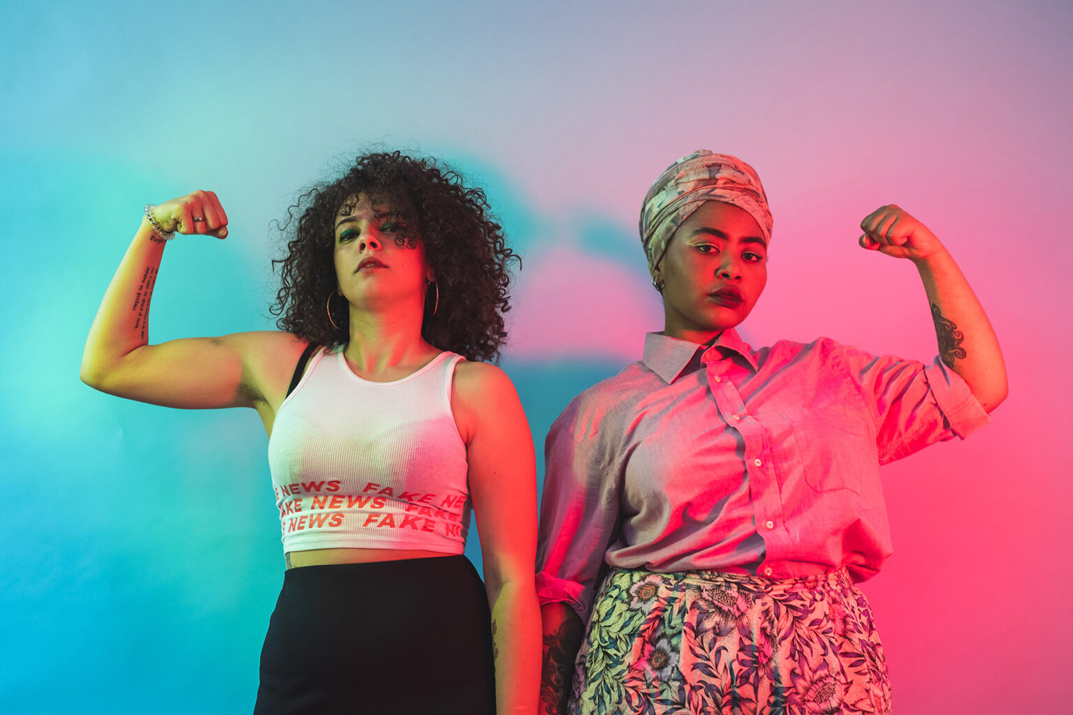 Two powerful-looking women flexing their muscles in the style of Rosie the Riveter on a blue and pink background.