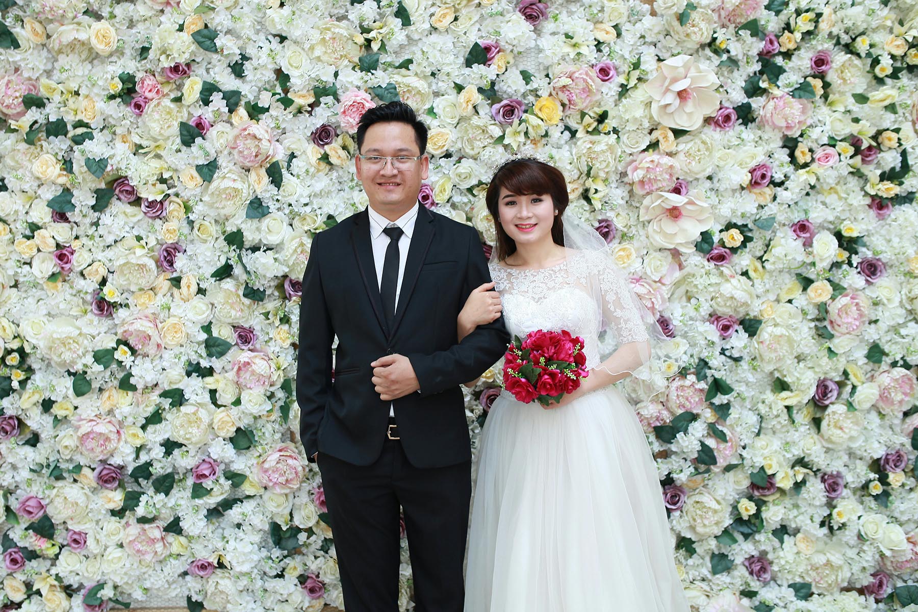Soon-to-be married couple standing in front of a flower wall.