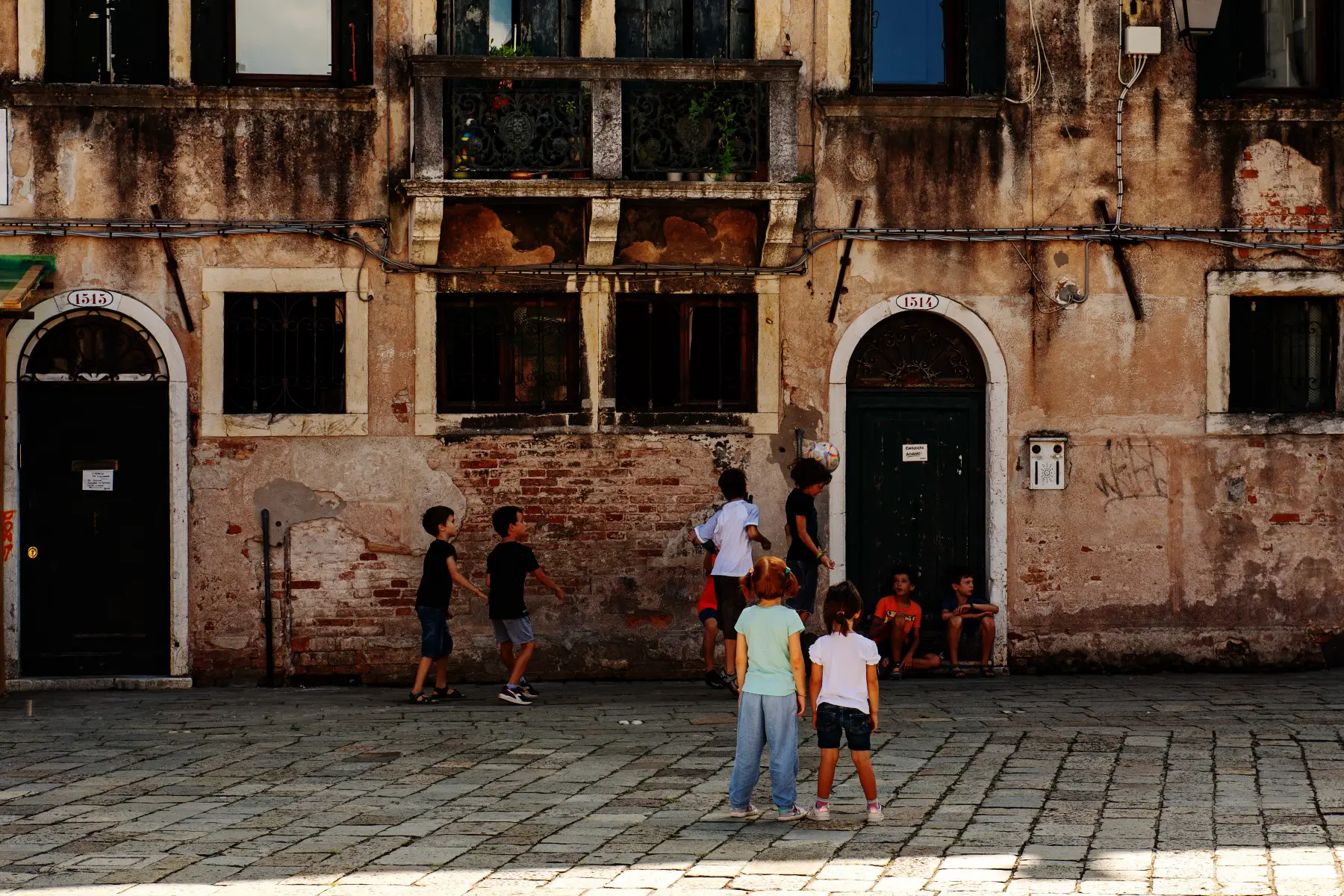 A group of children playing football (soccer) in the shade in a city square in Venice, Italy