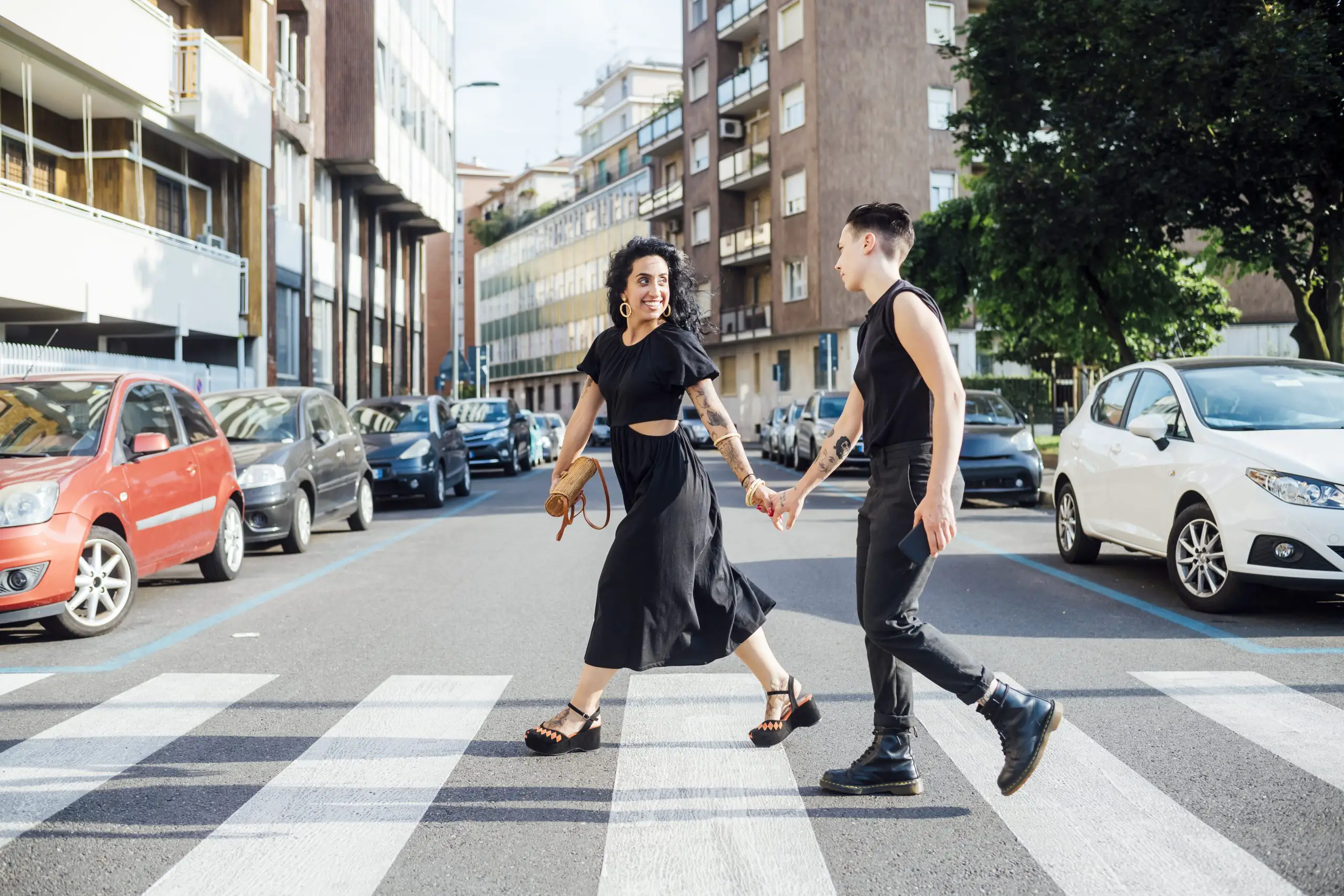 Cute couple in black crossing the road with zebra crossing, holding hands.