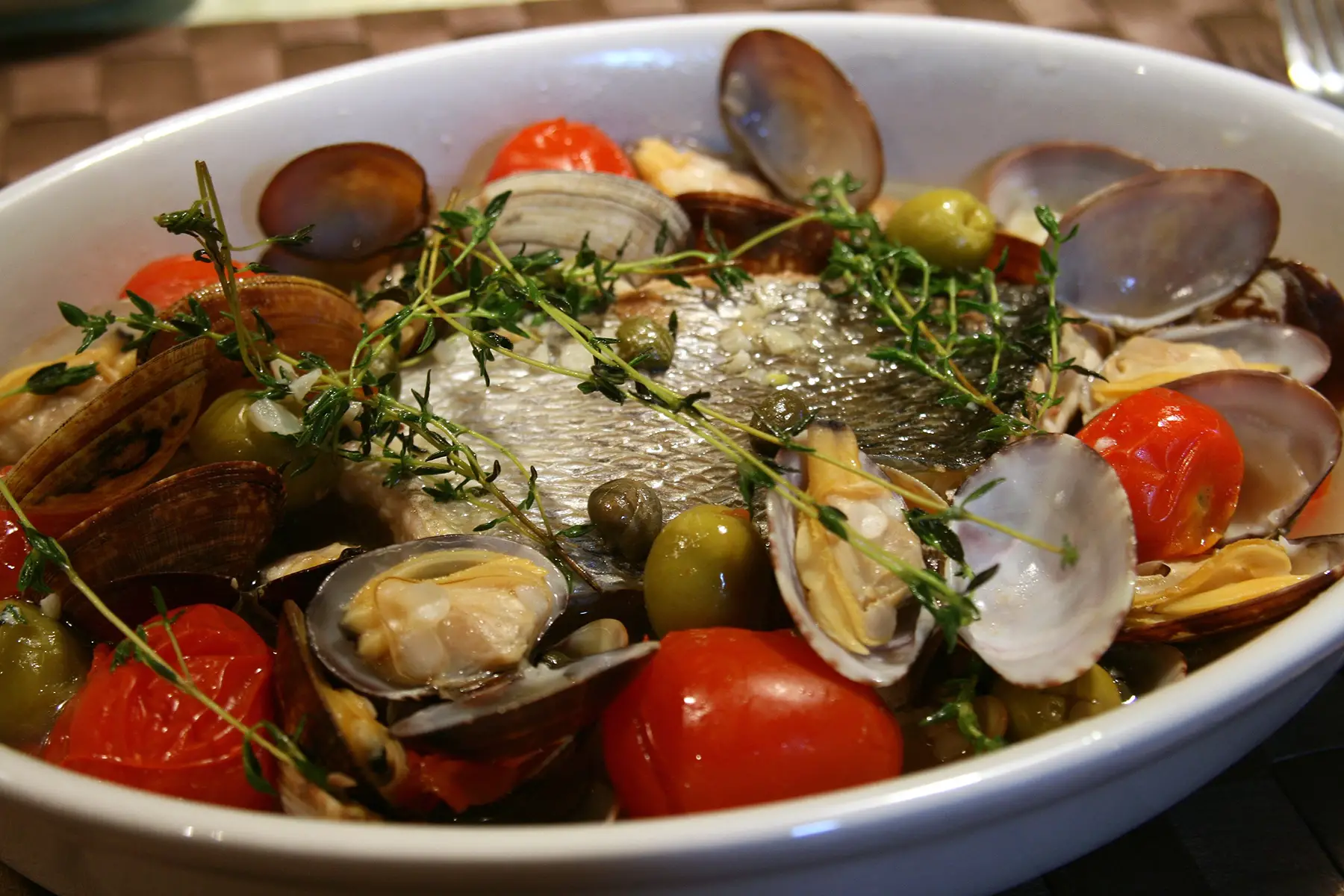Acqua pazza – a piece of fish in a dish surrounded by tomatoes, olives, mussels, and herbs