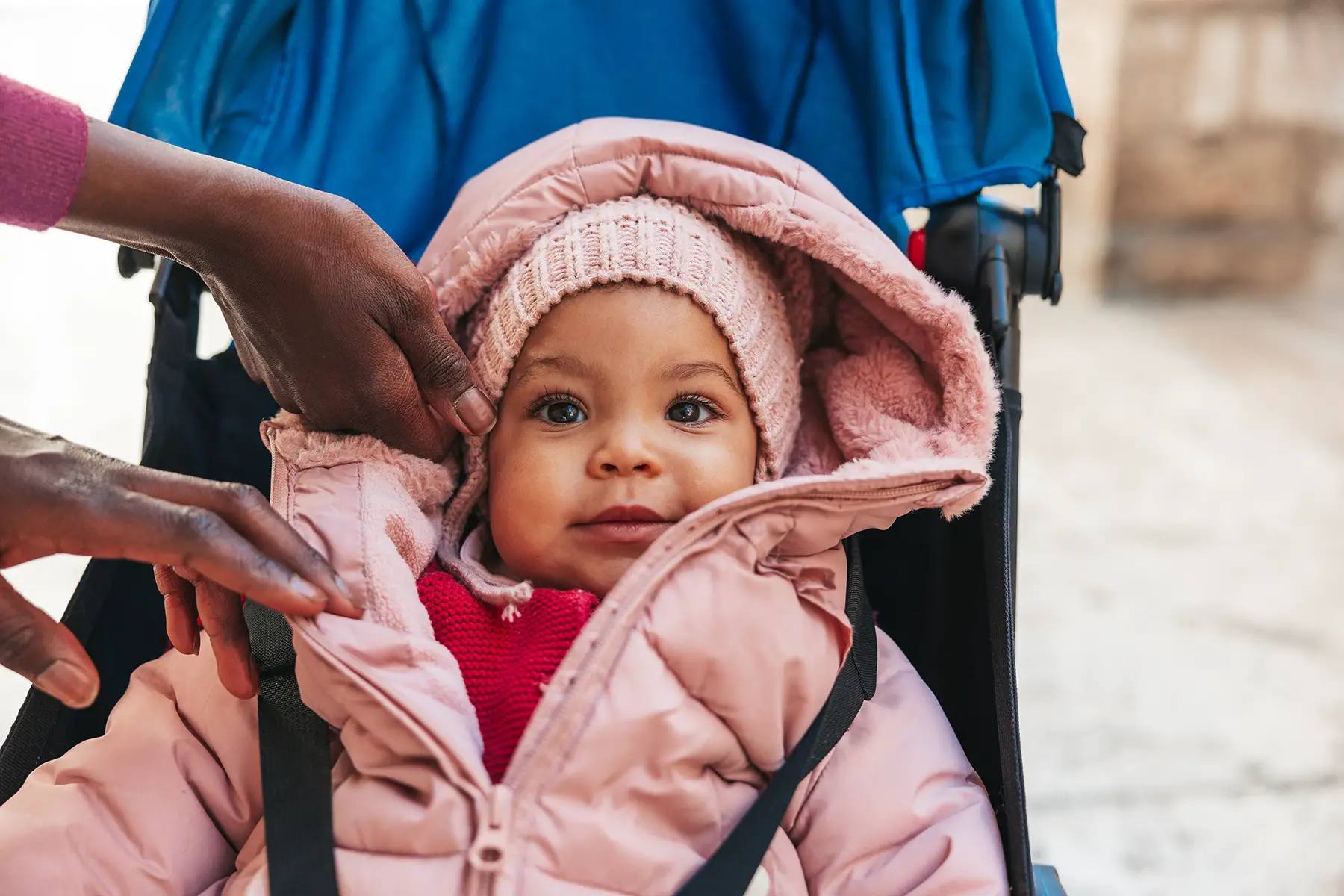 A baby wrapped up in a pink puffer jacket in a pram