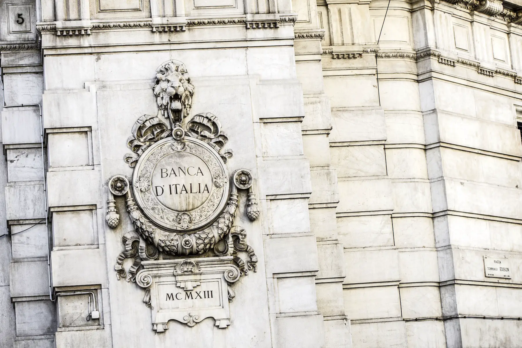 Close-up of a decorated Banca D'Italia sign on the wall of an old white building