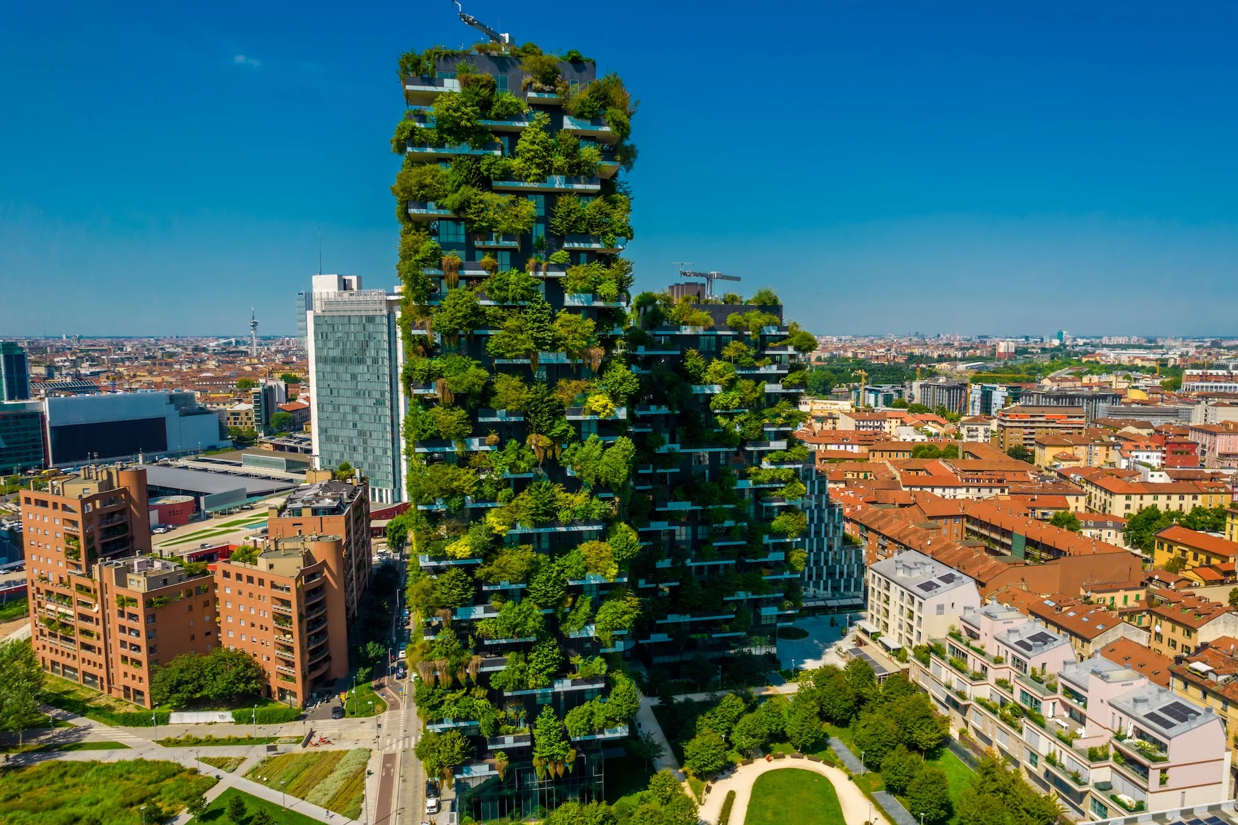 Two modern apartment buildings covered in greenery stand tall against the Milan skyline