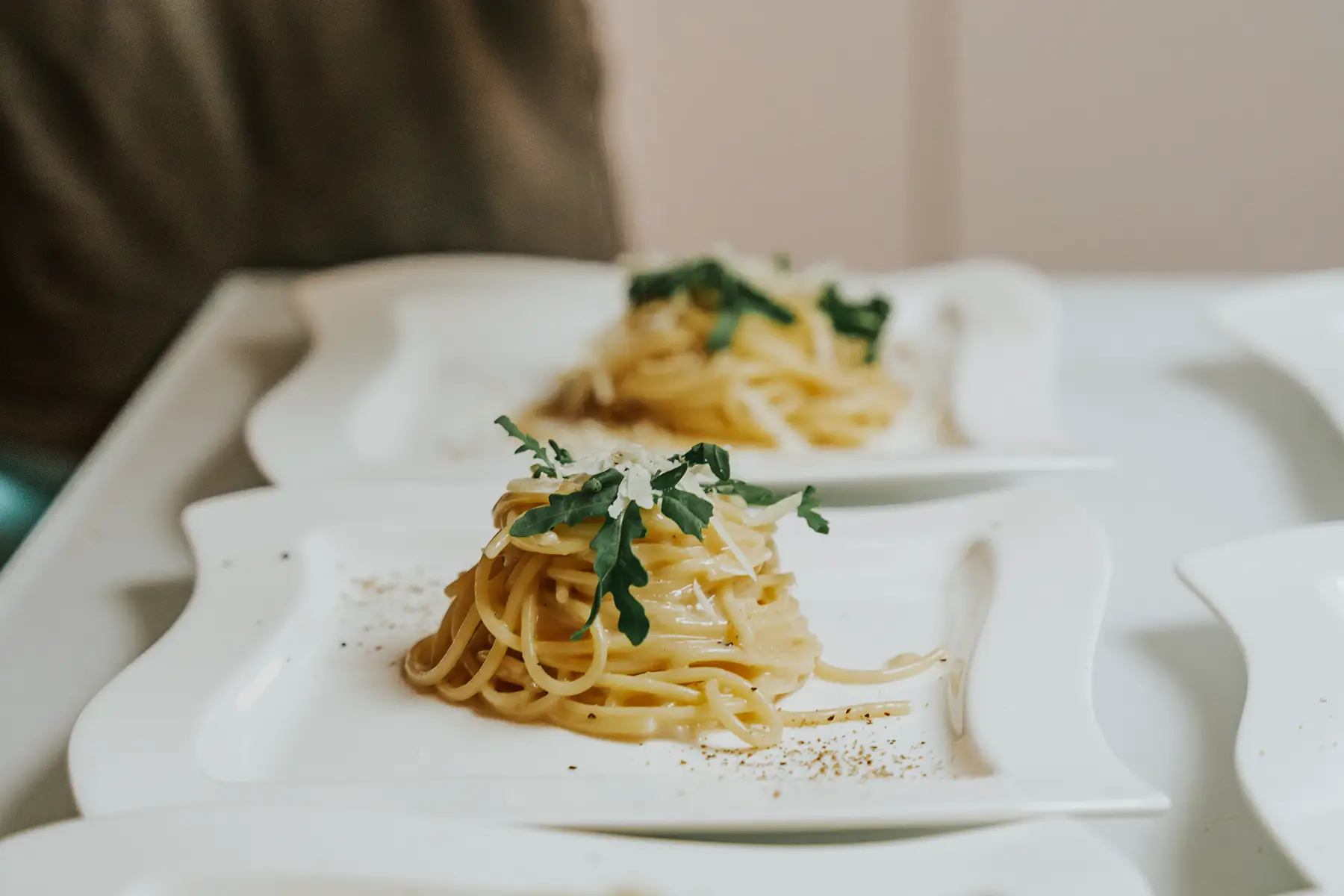 Cacio e pepe: small mound of pasta with pepper, cheese, and herbs on a square white plate