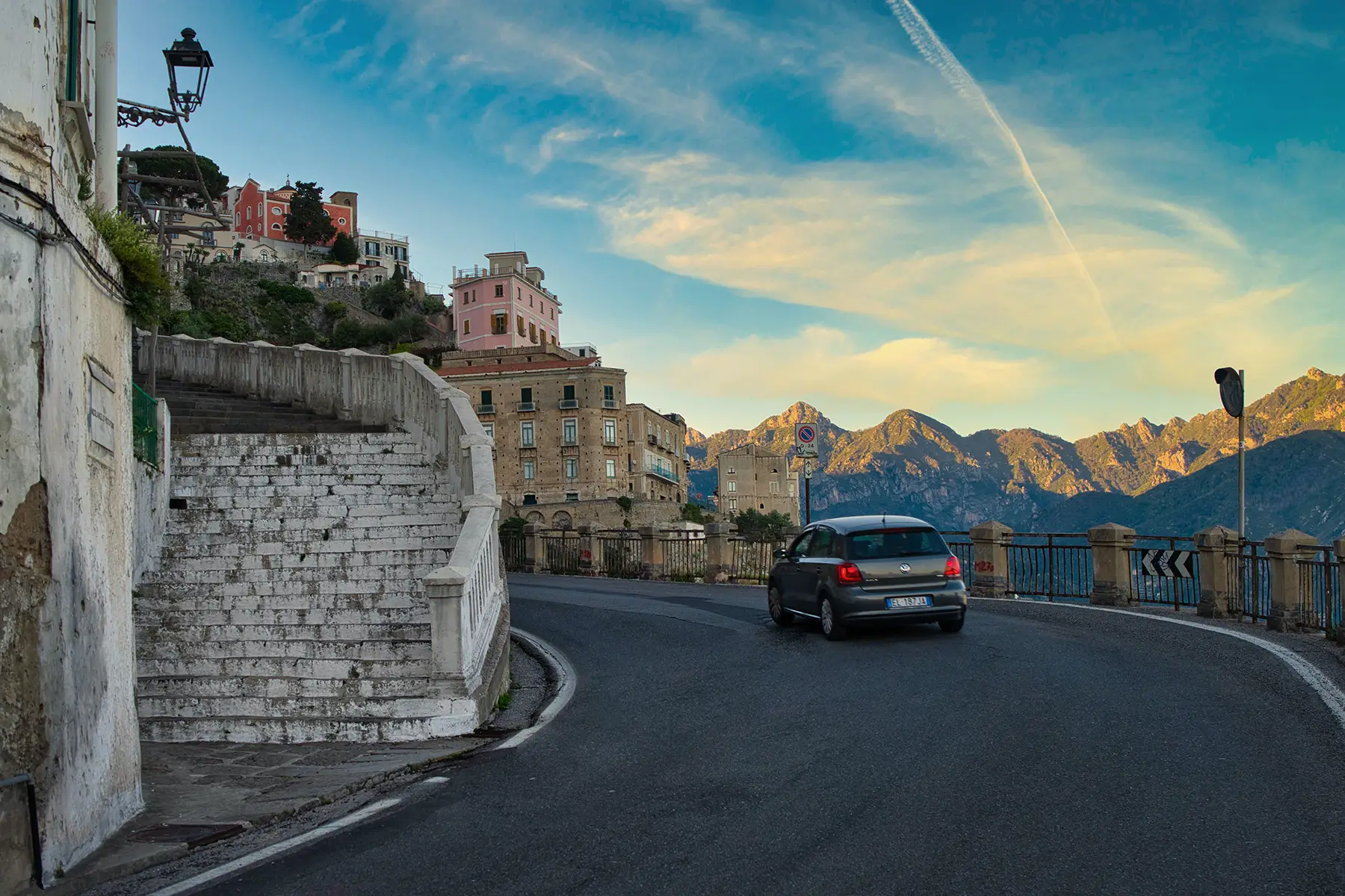 A car takes a curve on a beautiful mountain road with old Italian houses lining the street