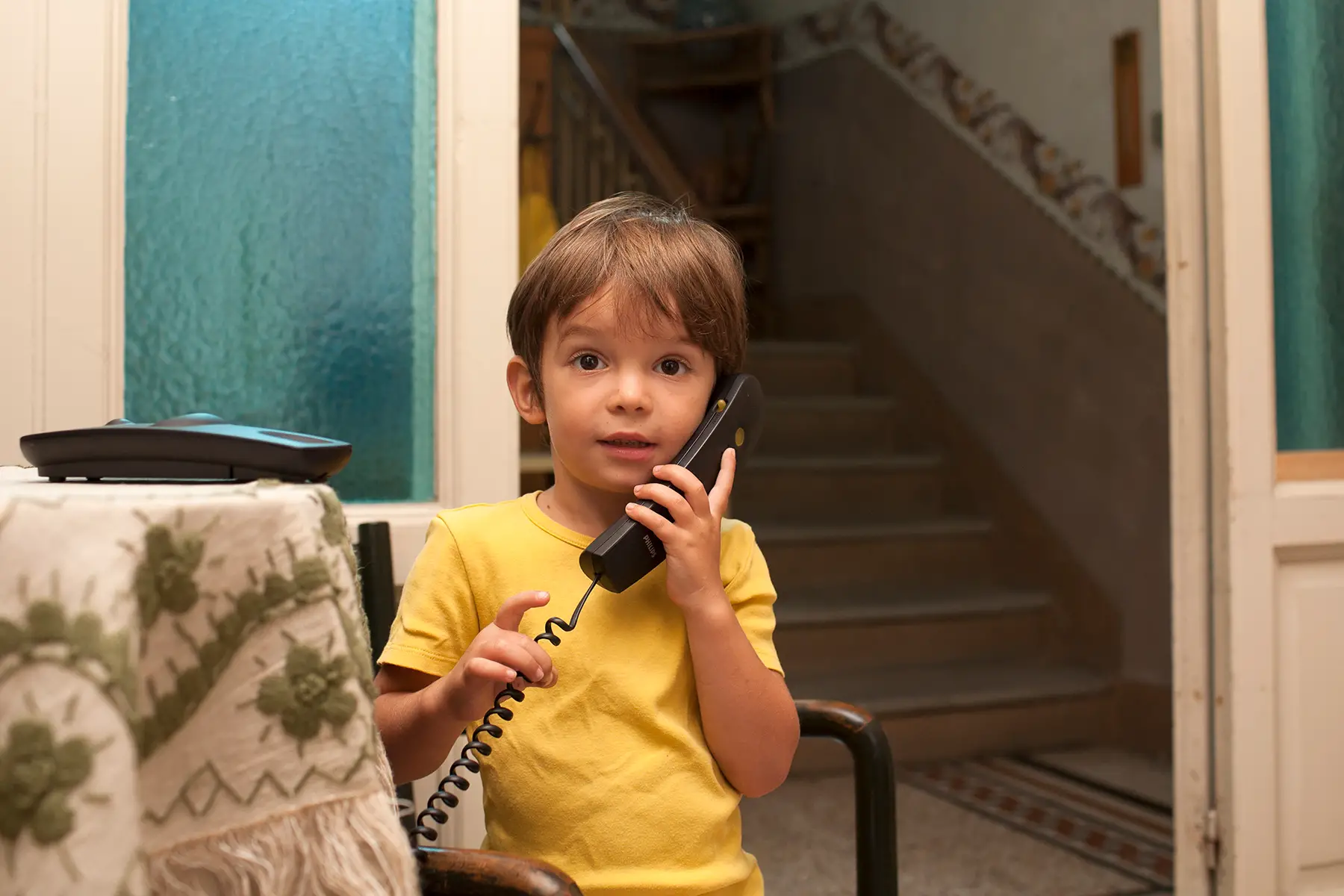 A young boy making a call on a landline phone in his living room