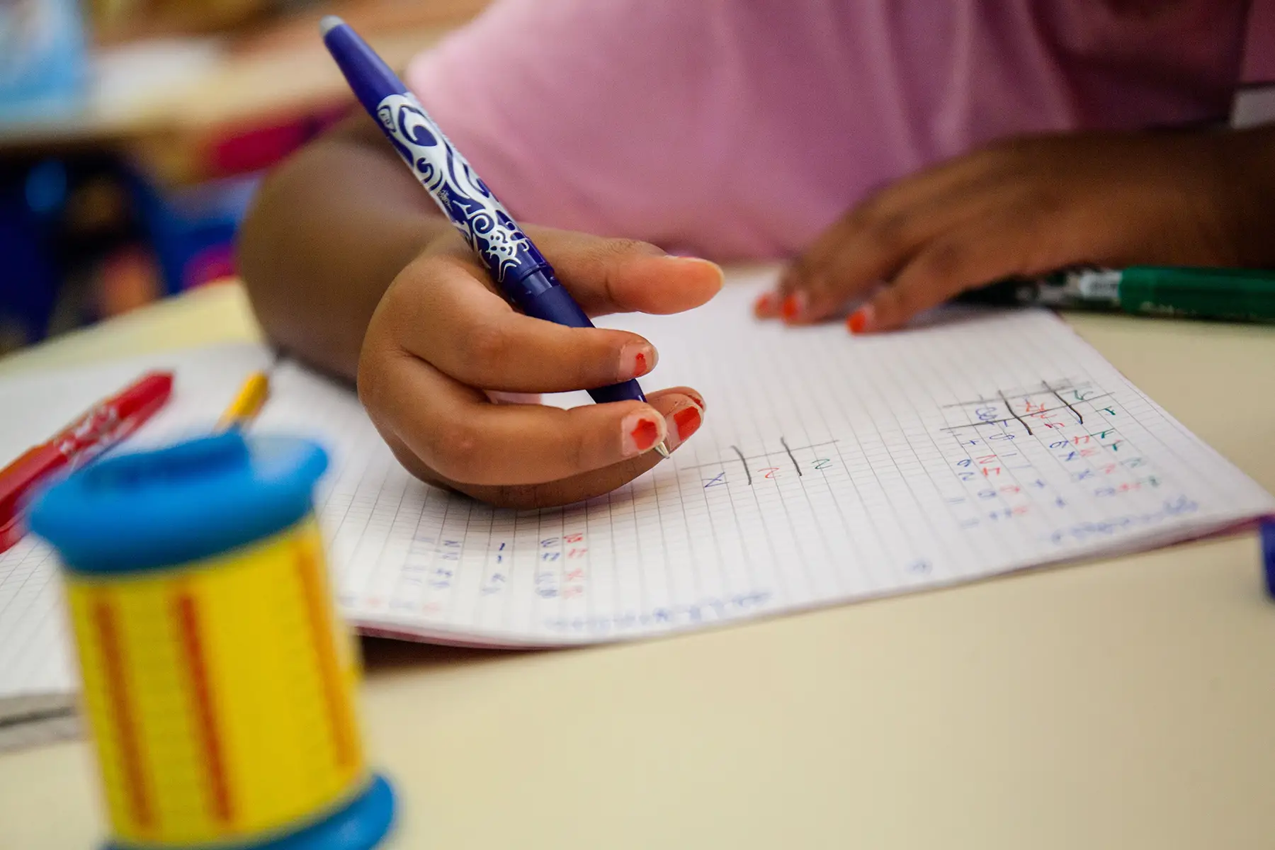 A close-up of a child writing in a math exercise book