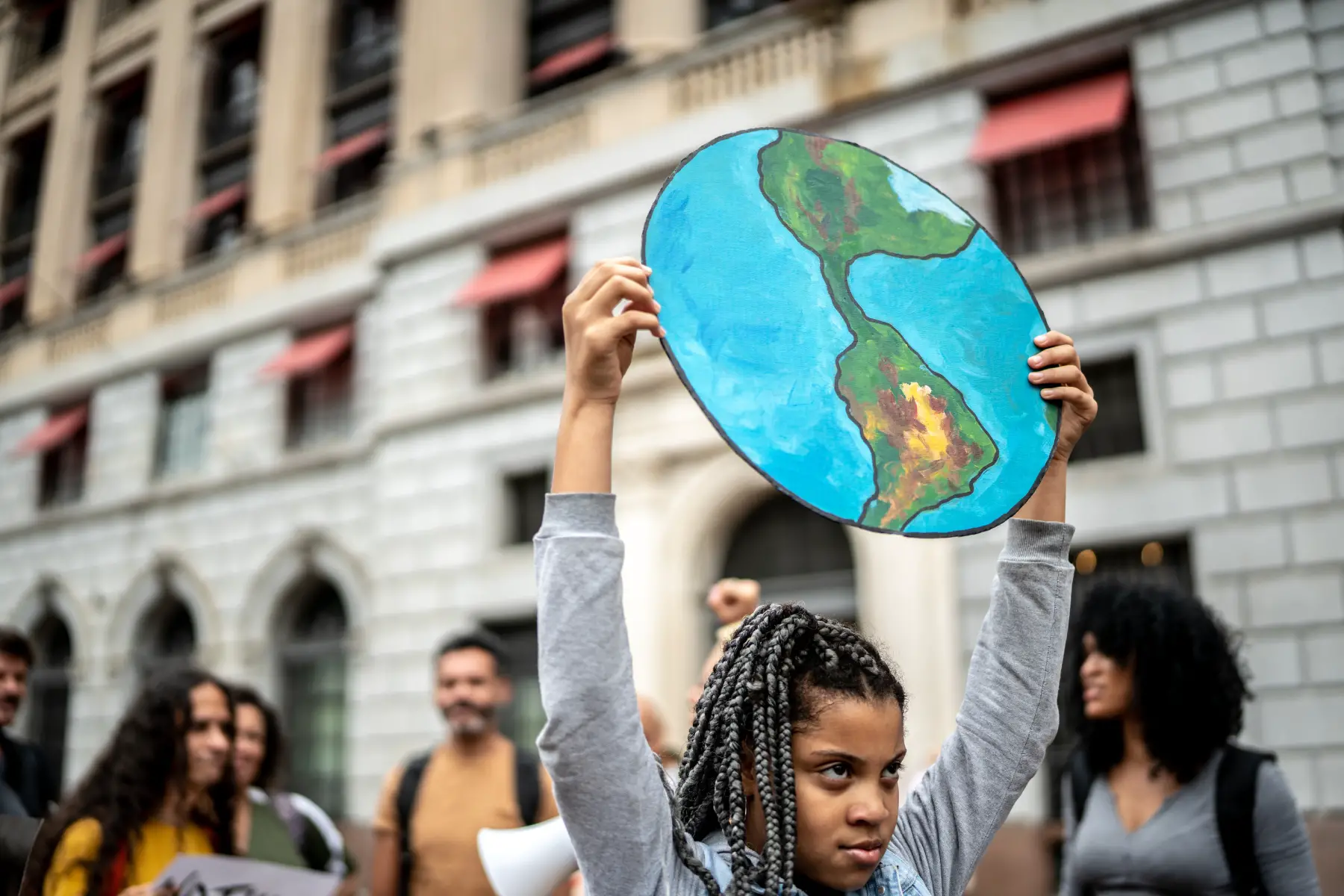 Teen girl at a climate/environmental protest holding a sign in the shape of the earth
