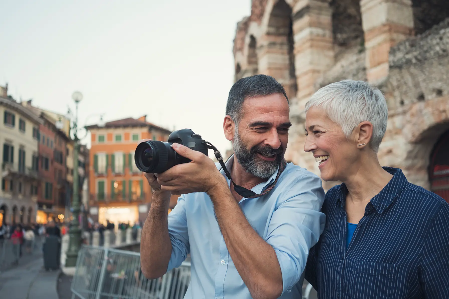 A couple, possibly retired, smiling at each other. One is pointing a camera at something.