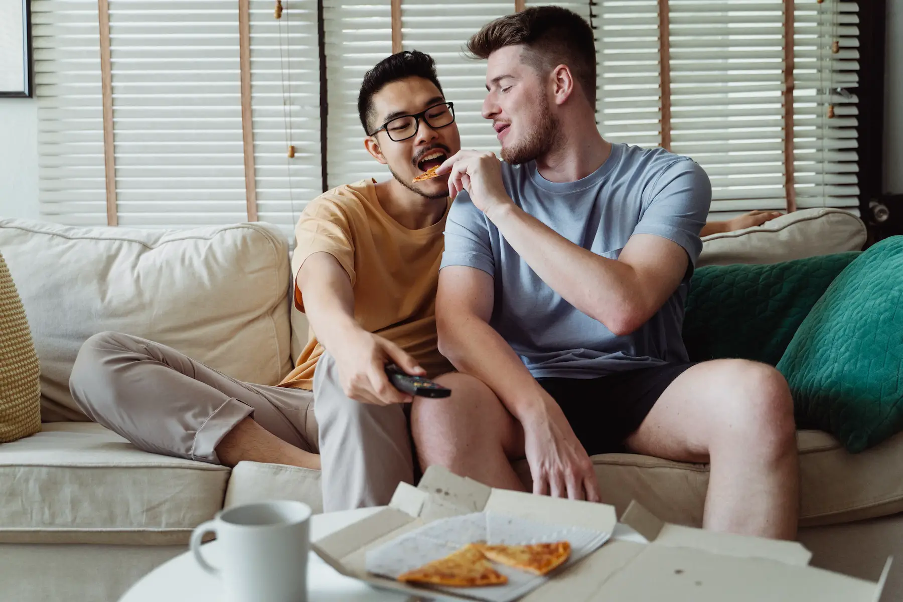 A man feeds his partner pizza on the couch