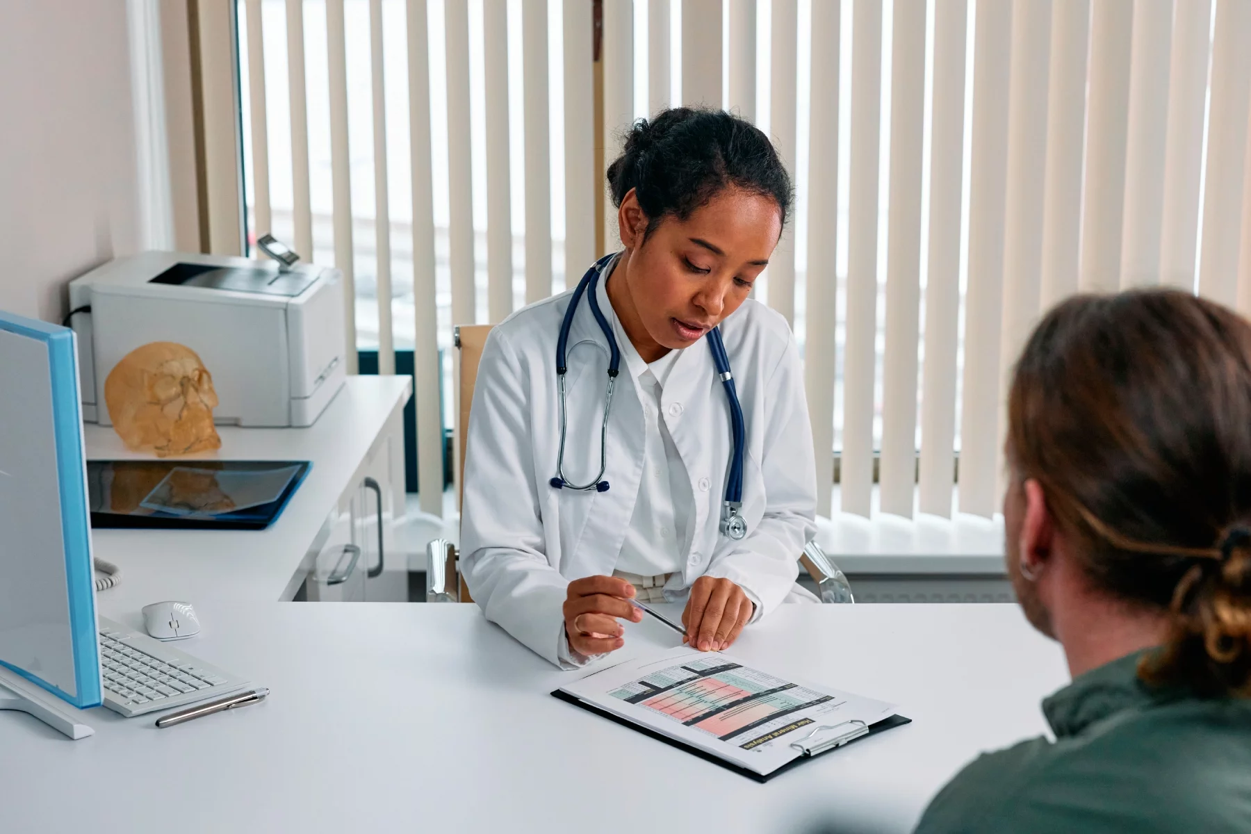 Doctor consulting a patient across a desk while reading from their chart