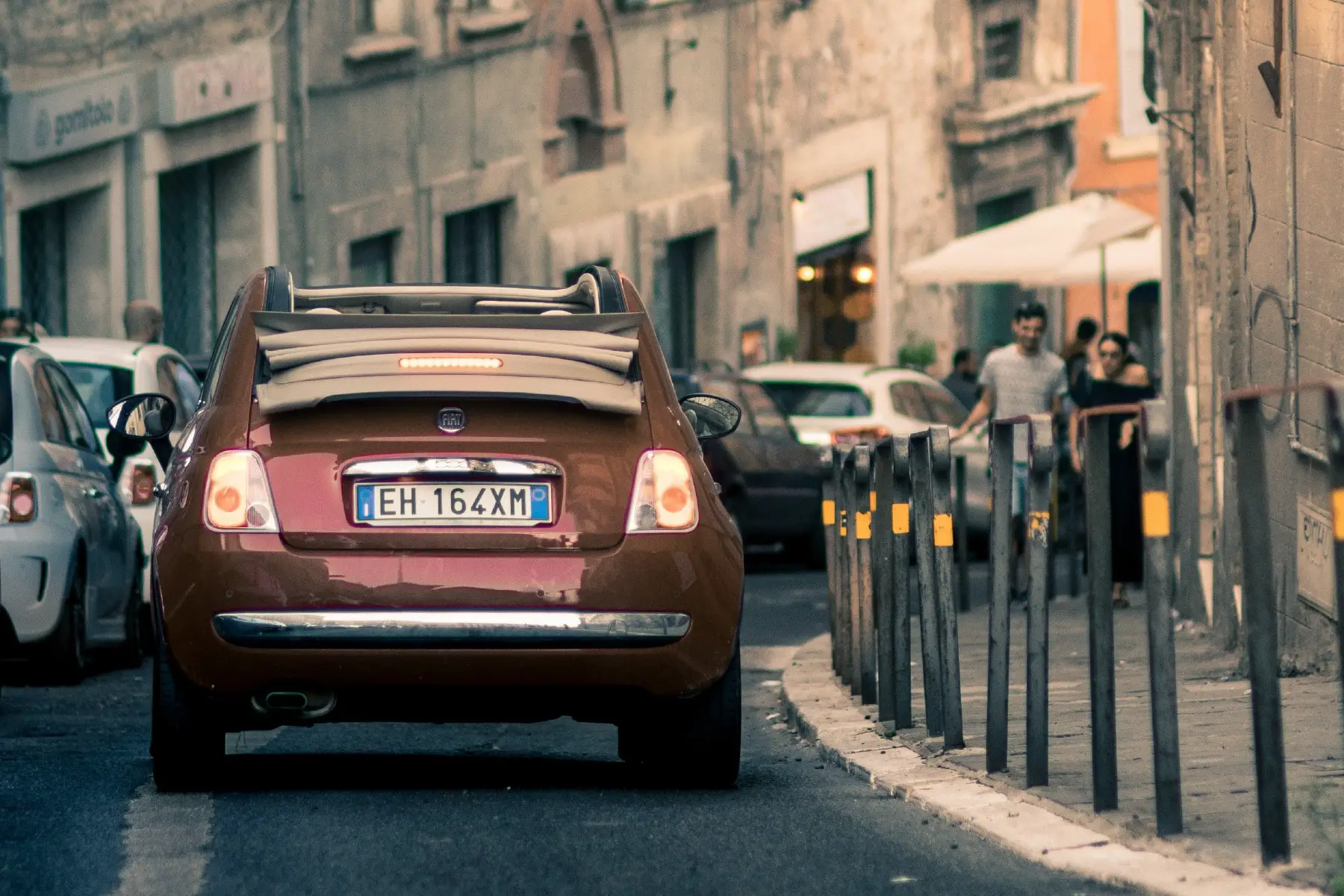 A red Fiat driving along a narrow street lined with parked cars in Perugia, Italy