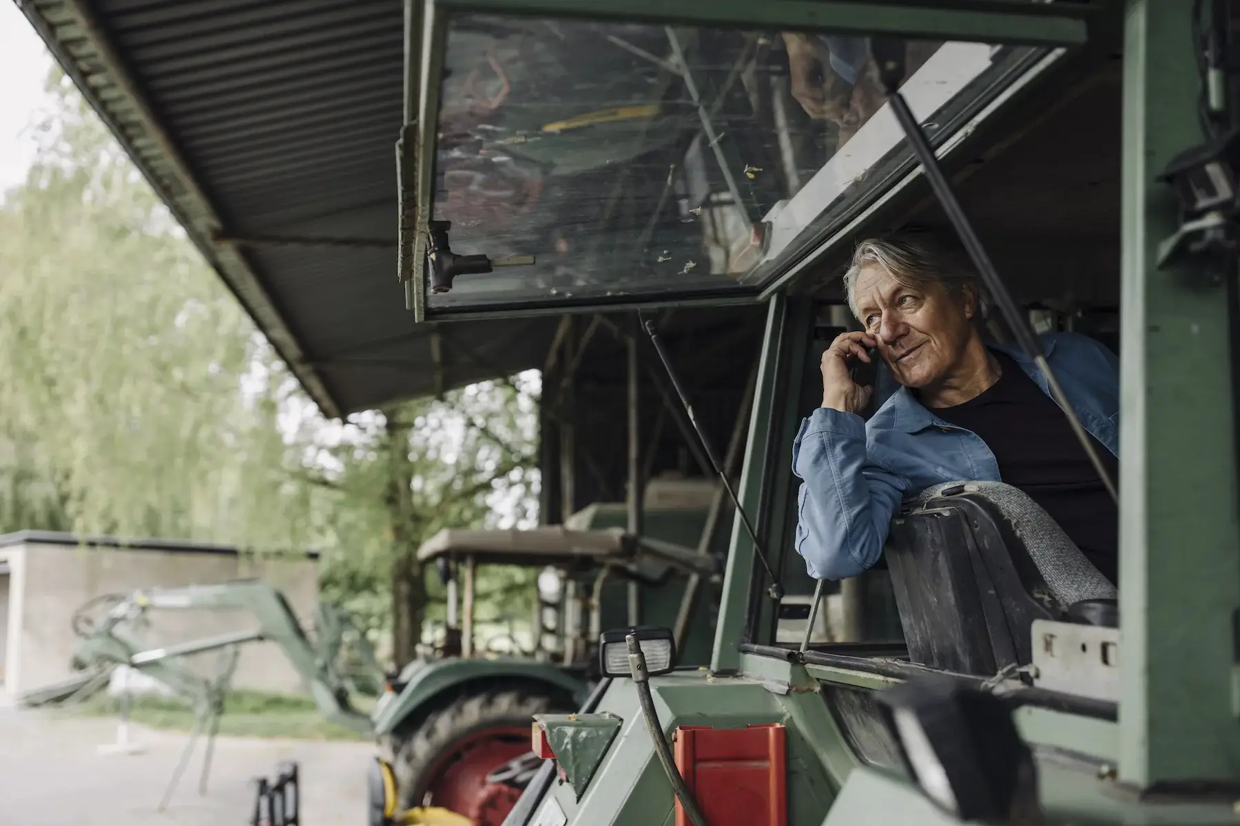 An farmer makes a phone call out the back window of his tractor