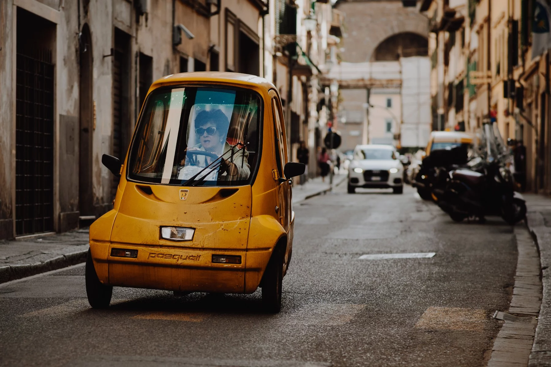 A woman driving a small three-wheeled yellow electric car down the street in Florence, Italy.