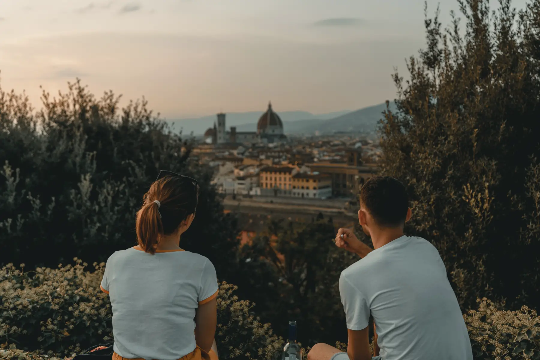 A young couple sitting on a hill overlooking Florence at sunset in summer.