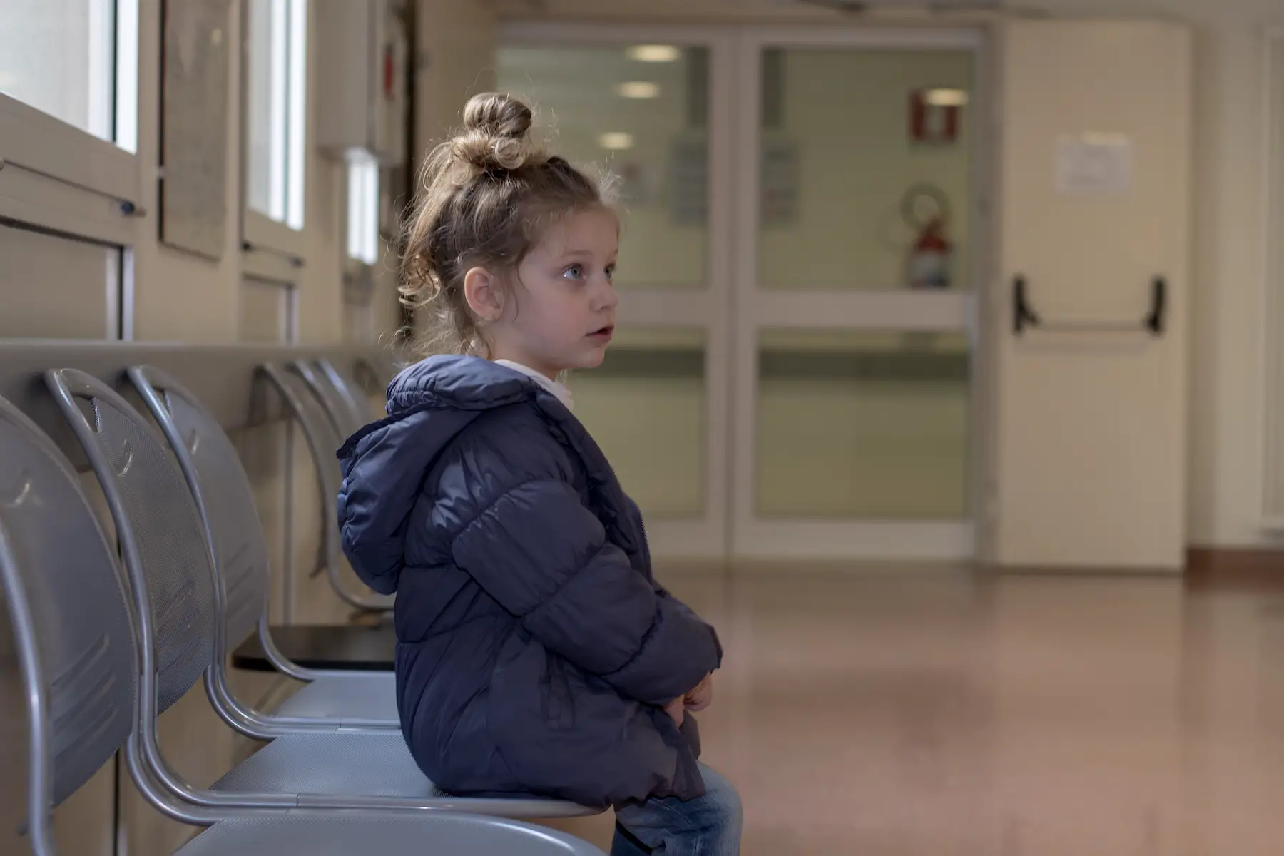 A little girl sits alone in the waiting room of a hospital's emergency room