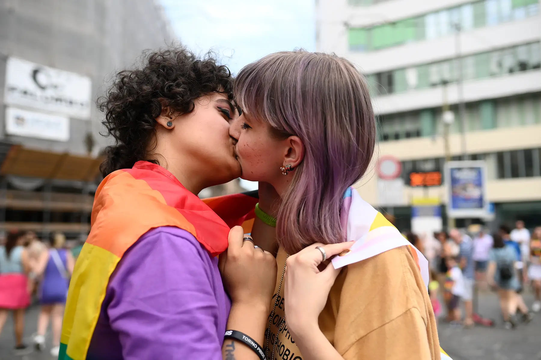 Young women kissing, wrapped in a rainbow flag