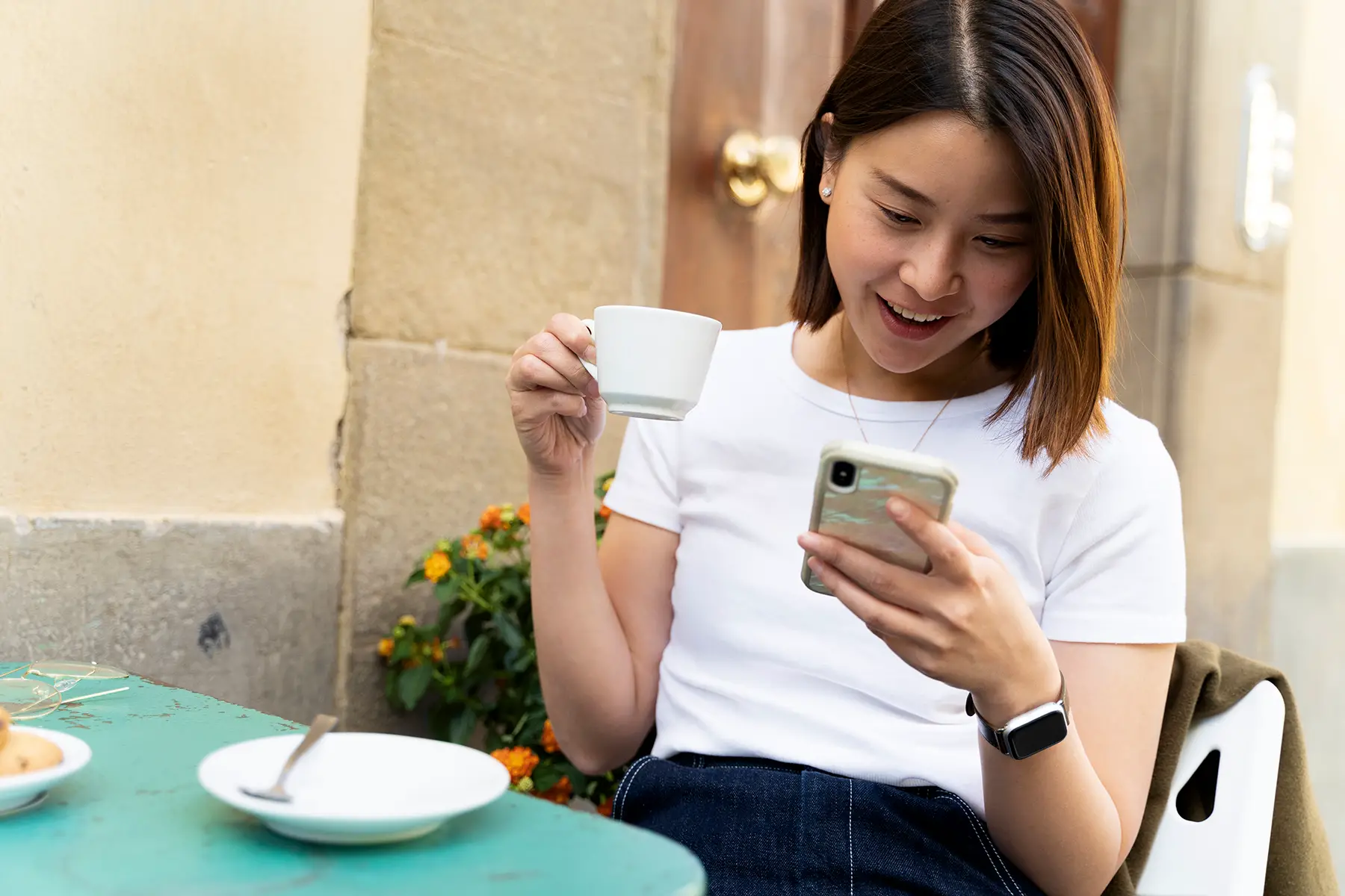 A woman looking down at her phone and smiling as she hold a cup of coffee