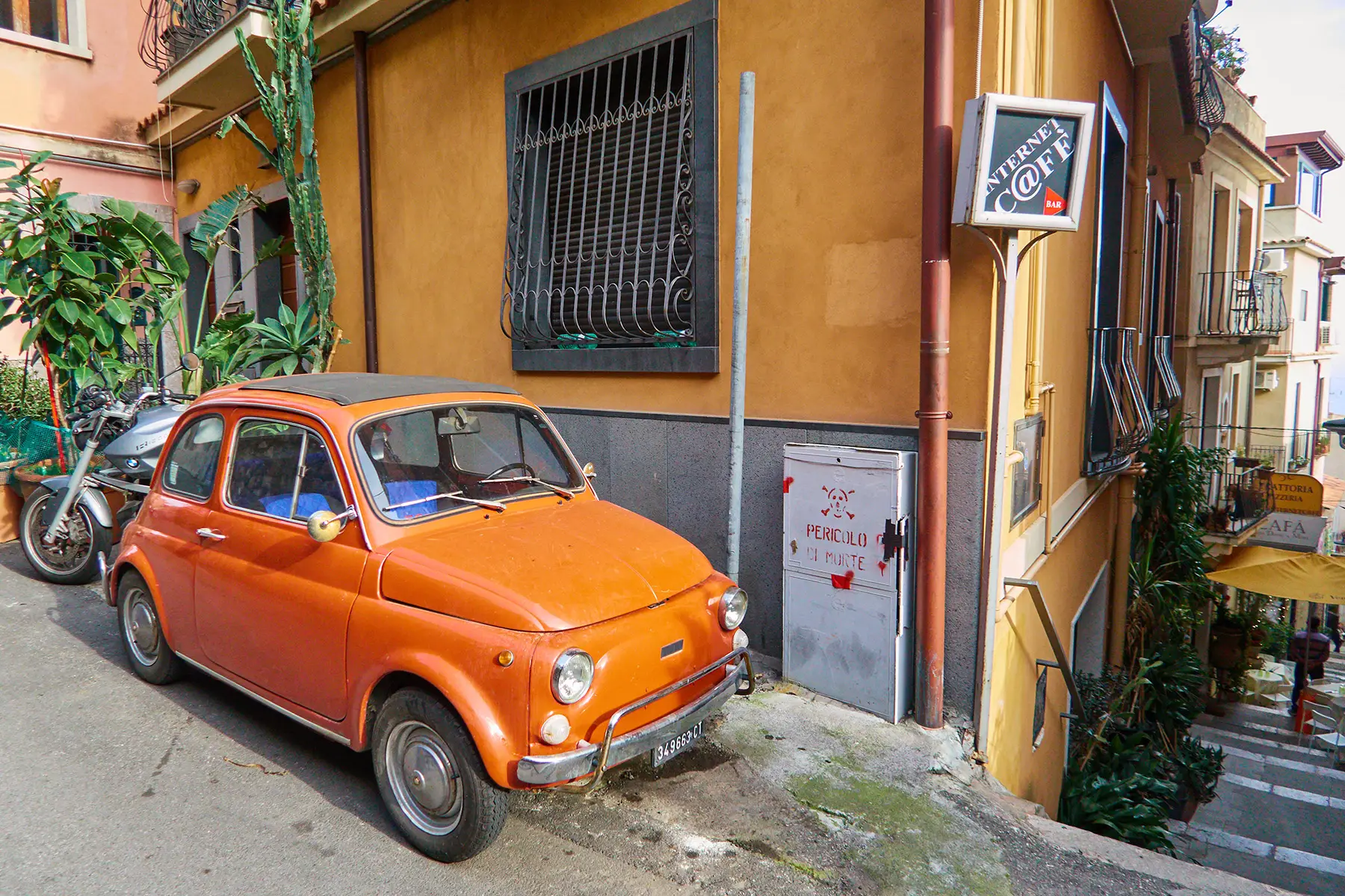An orange car parked outside a café with a small sign saying 'Internet c@fe'