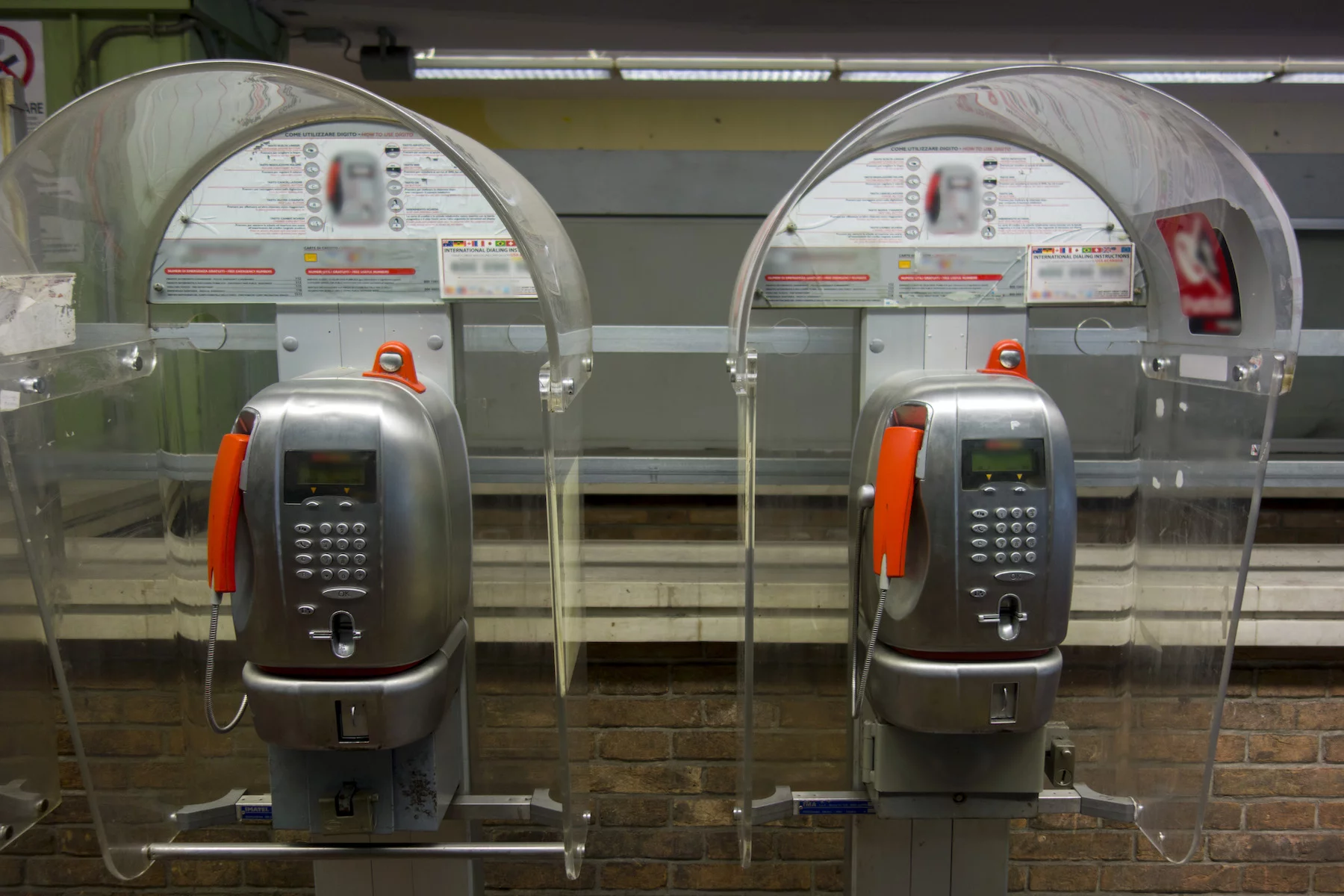 Two identical Italian public phones stand side-by-side against a brick wall