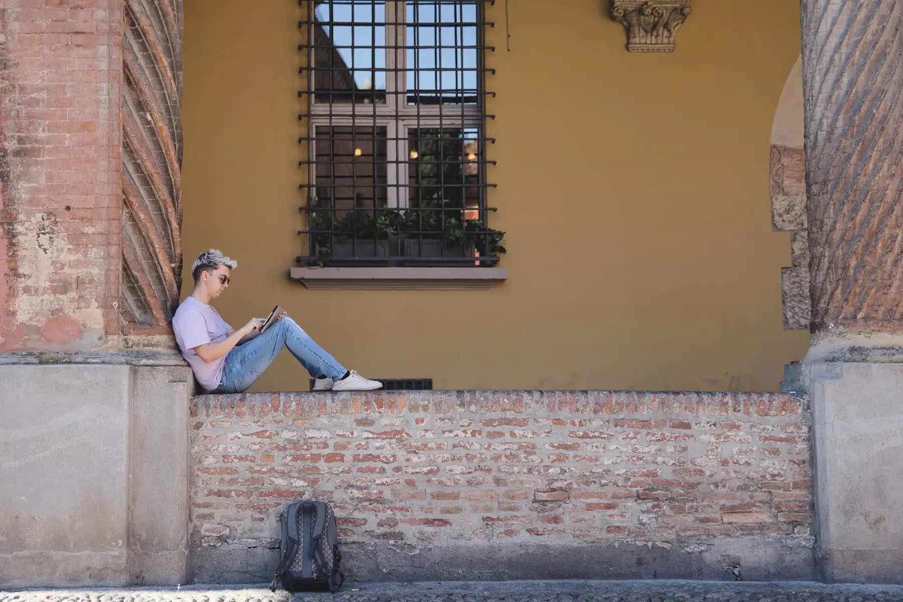 Young man studying with a tablet sitting on a wall at the University of Bologna, Italy.