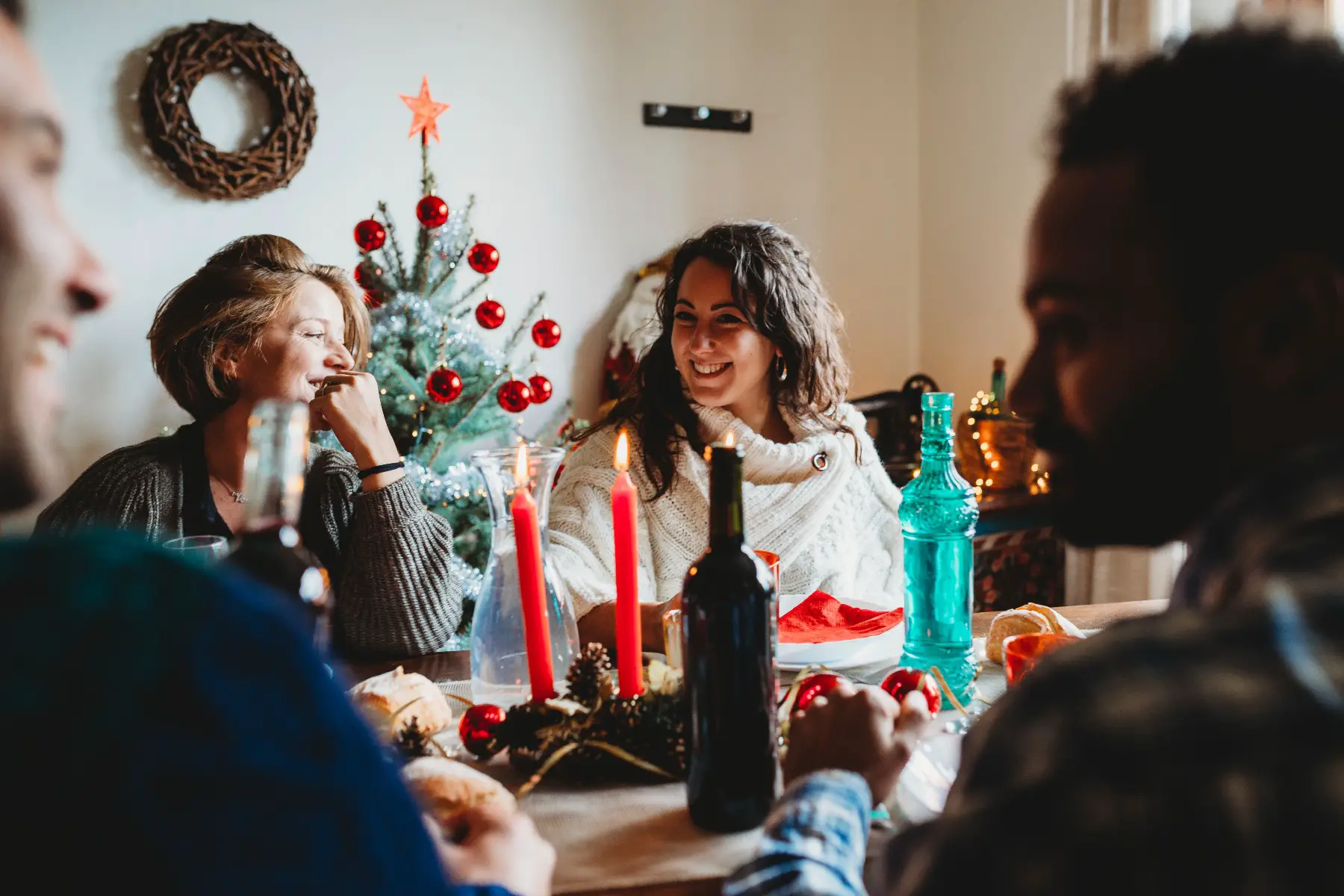 Happy family having Christmas lunch together. In the foreground, there is a silhouette of two men talking. The photo is focused on two women laughing.
