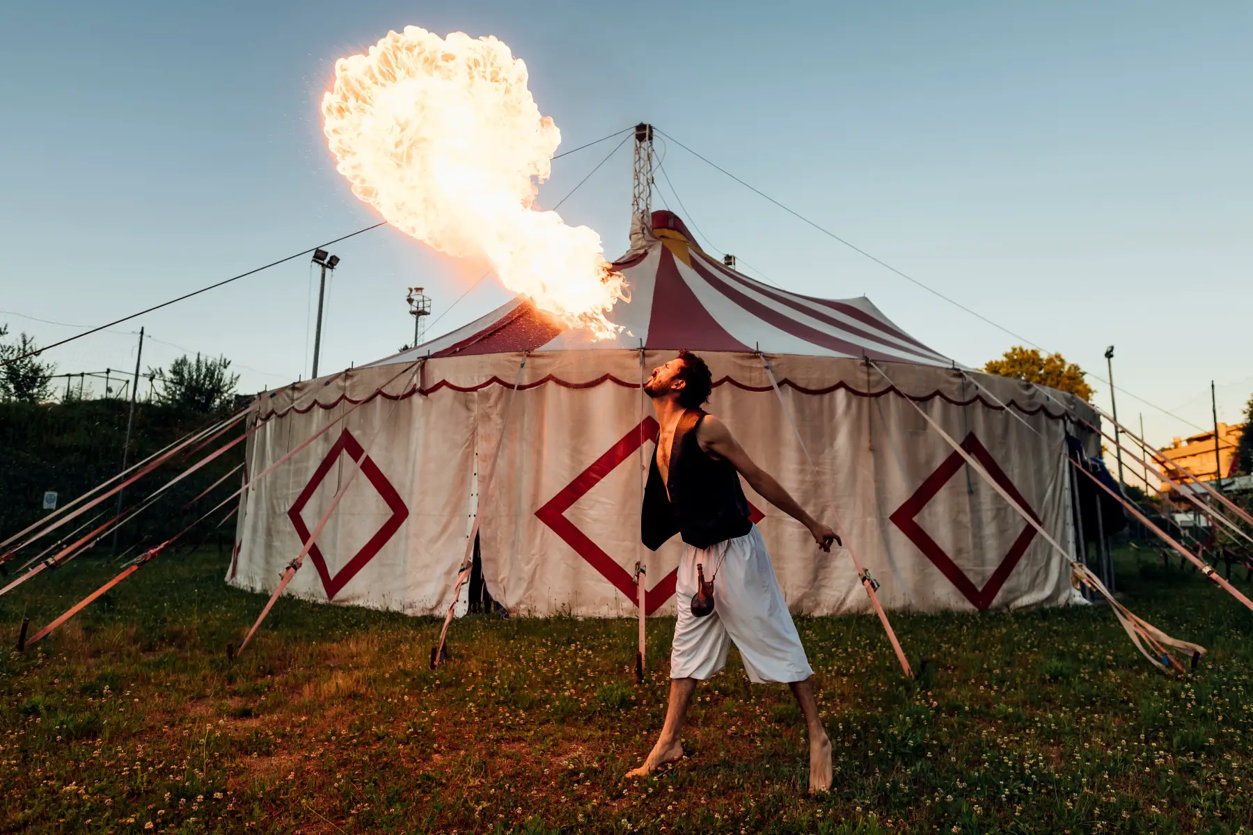 Man blowing fire in front of a circus tent.