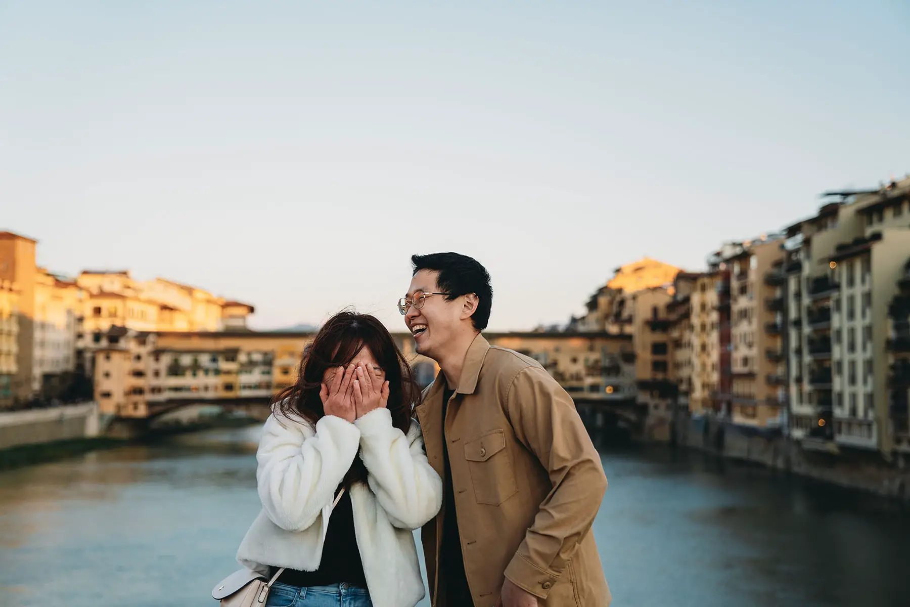 Cute couple is laughing together with Ponte Vecchio (Florence, Italy) in the background. The woman is hiding her face.