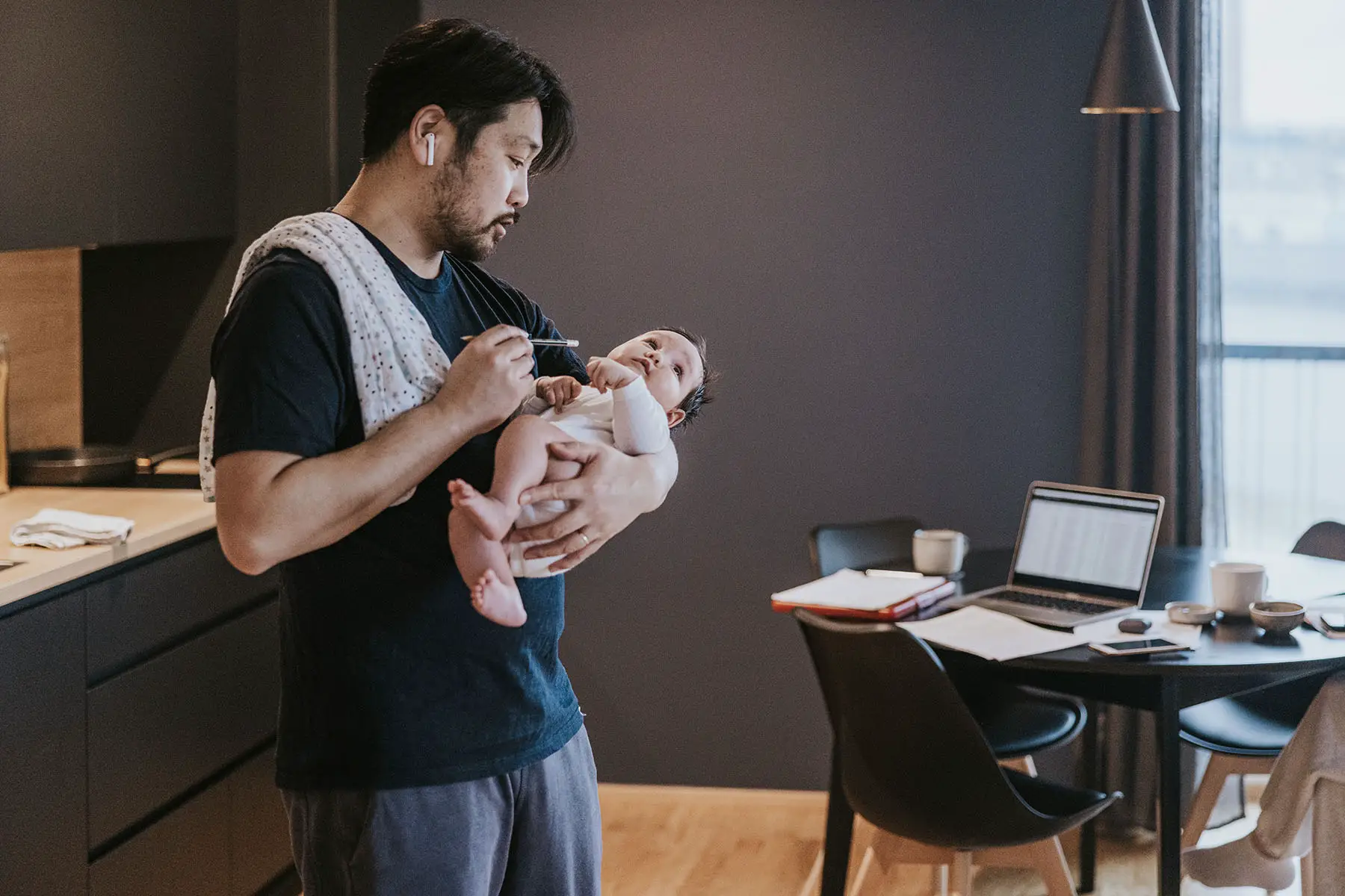 Father holding his baby girl while working from home with laptop.