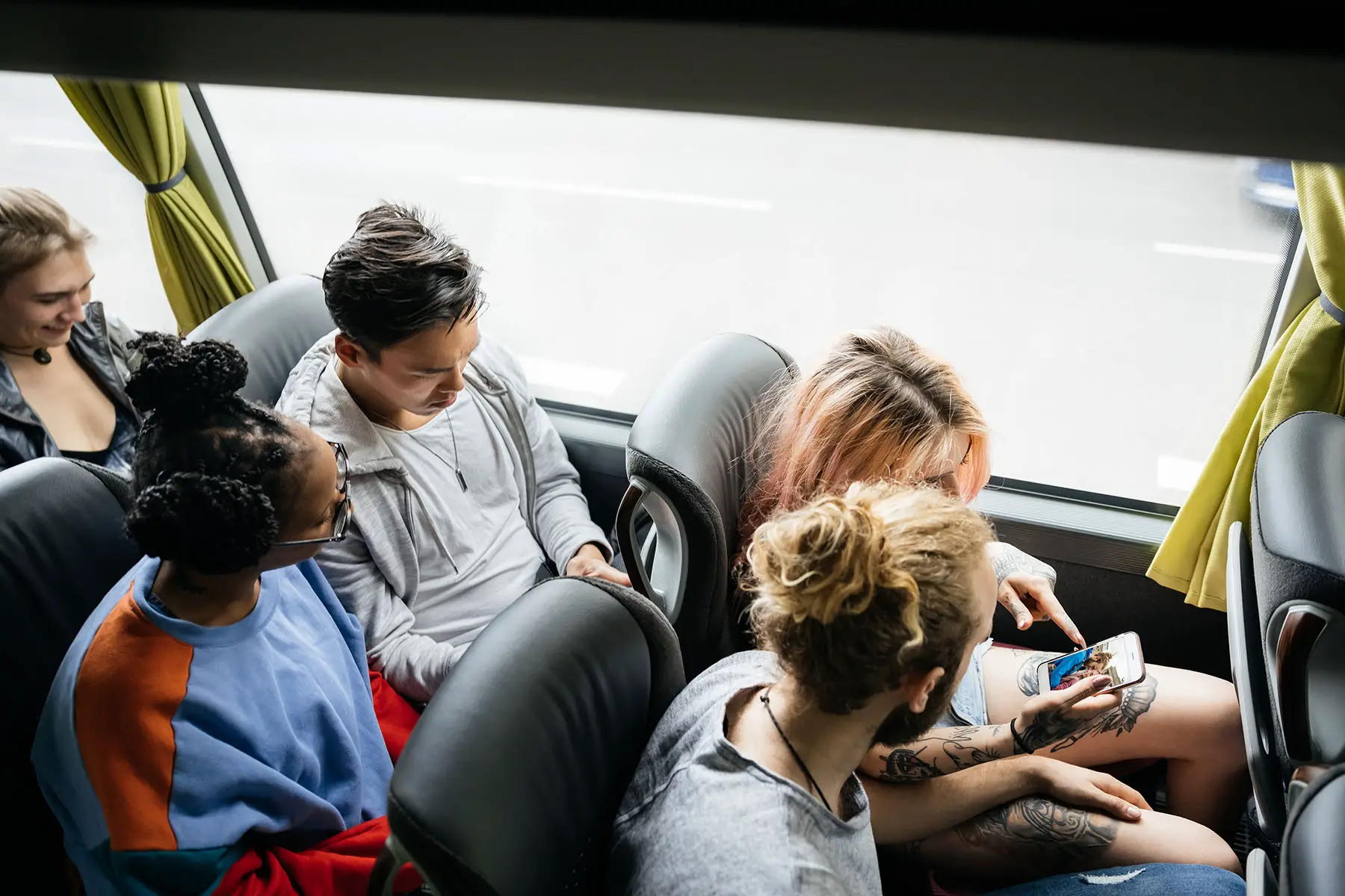 A young group of friends looking over recent photos of their travels as they journey together on a bus.