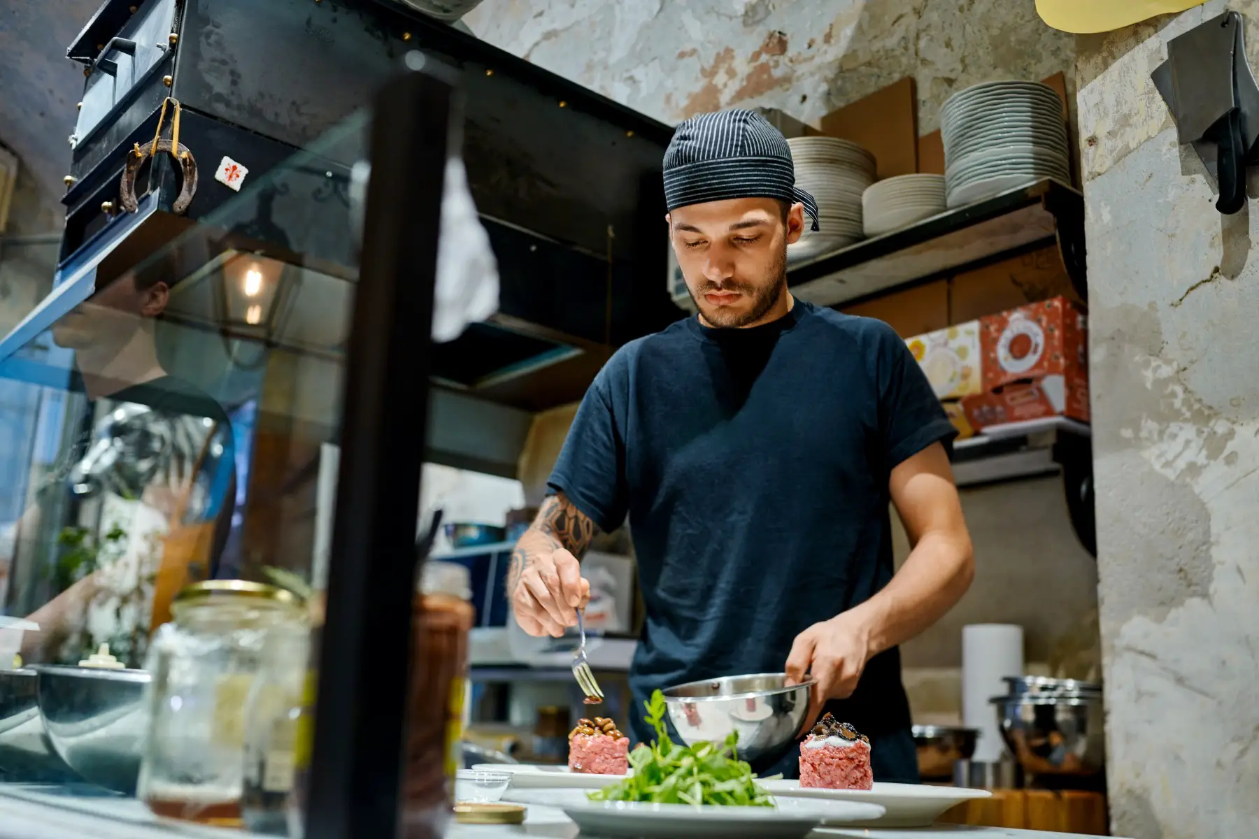A young man preparing a steak tartare dish in a commercial kitchen