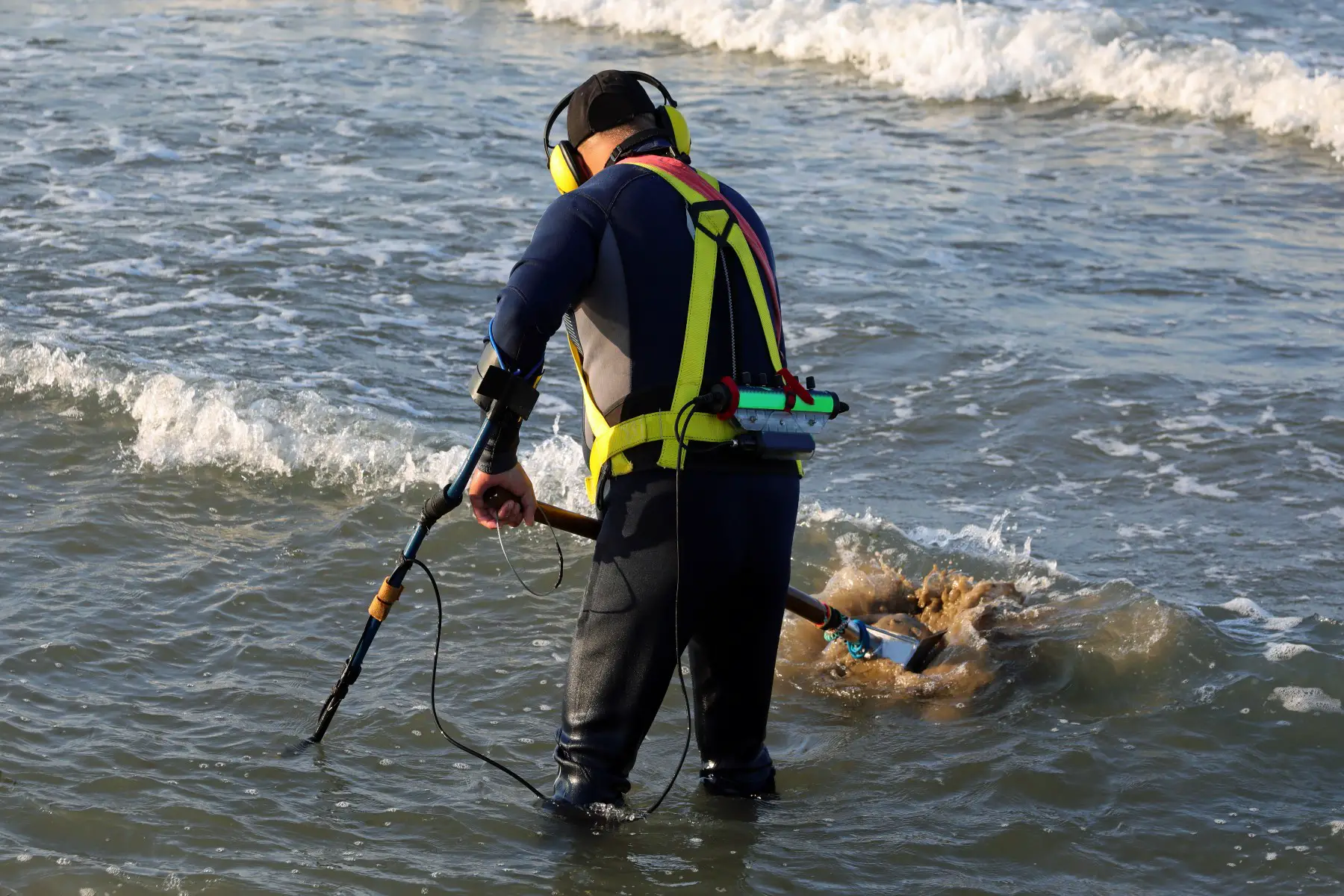 Man using a metal detector to recover lost items in the sea near the beach.