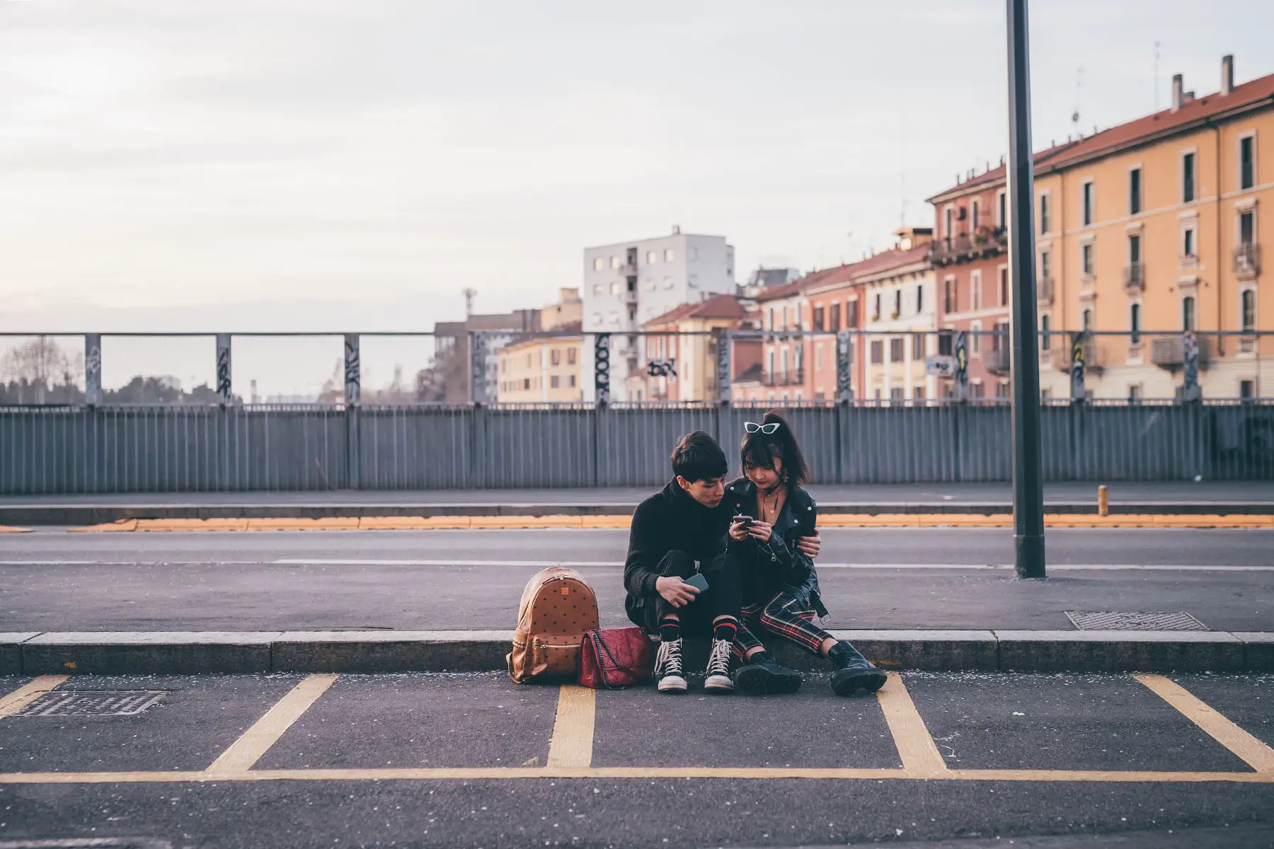 Couple looking at a smart phone while sitting on the curb in Milan, Italy.