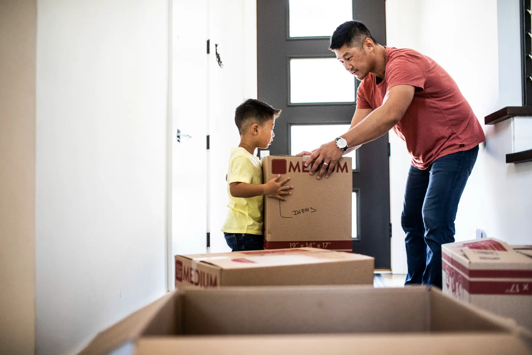 Father is handing a moving box to his son as they move in to a new home.