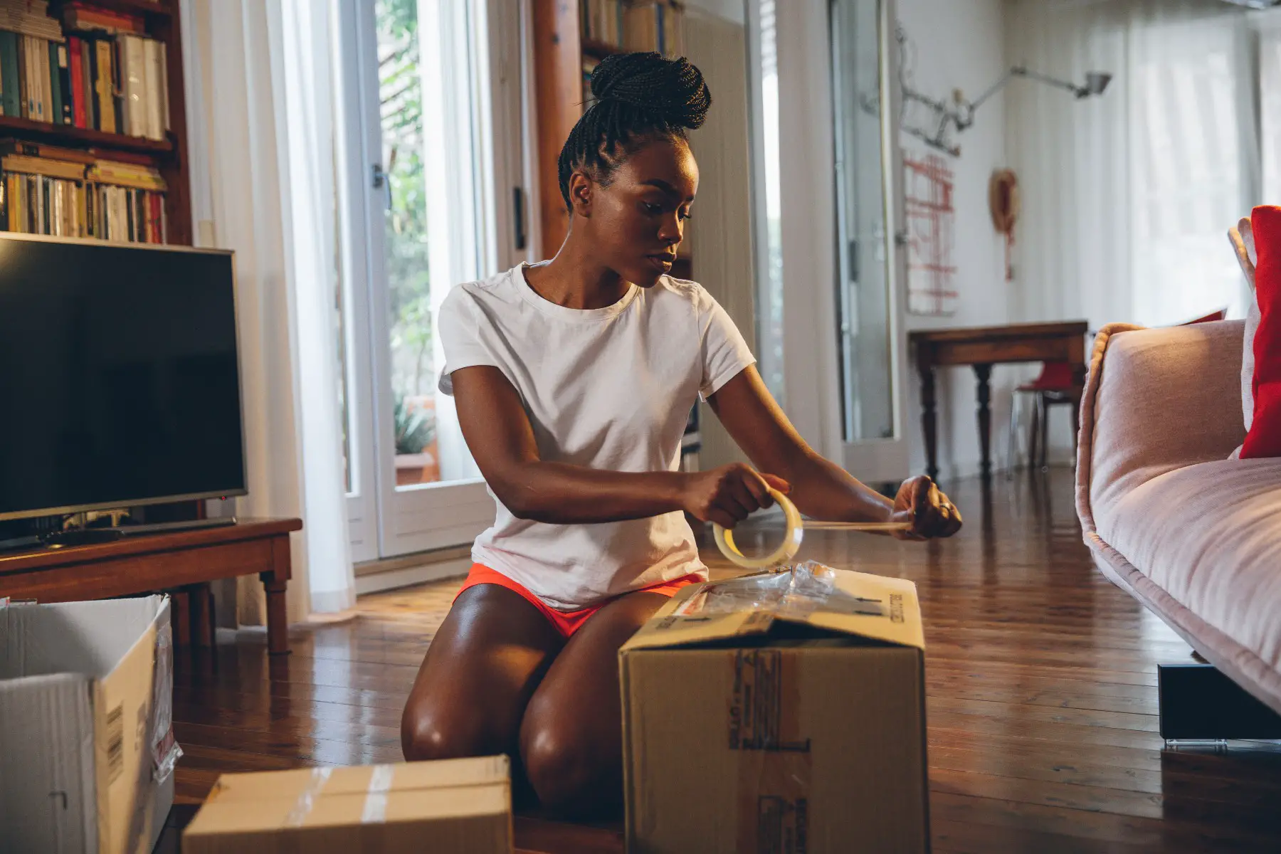 Young woman packing up her apartment and using plastic tape to close a cardboard box.