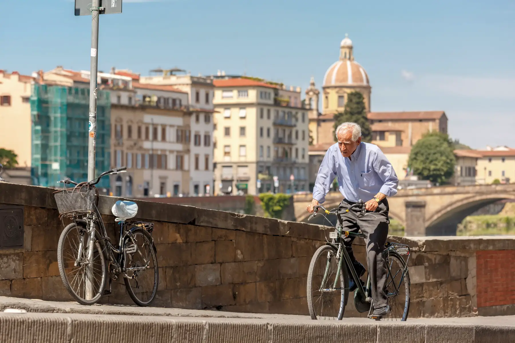 An older adult cycling on the quay of the river Arno in Florence, Italy