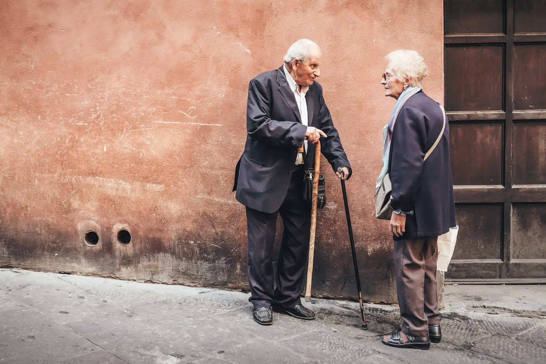 Two older Italian adults stop to have a conversation on the streets of Sienna, Italy.