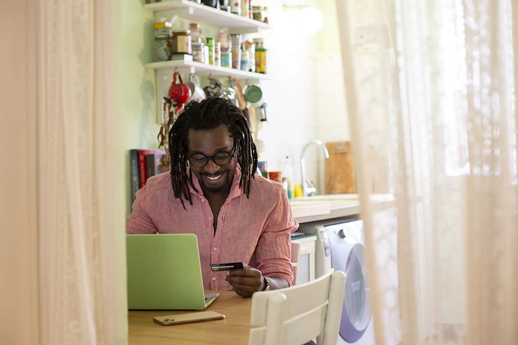 Man sitting at the kitchen table, smiling, as he enters his credit card info on a laptop.